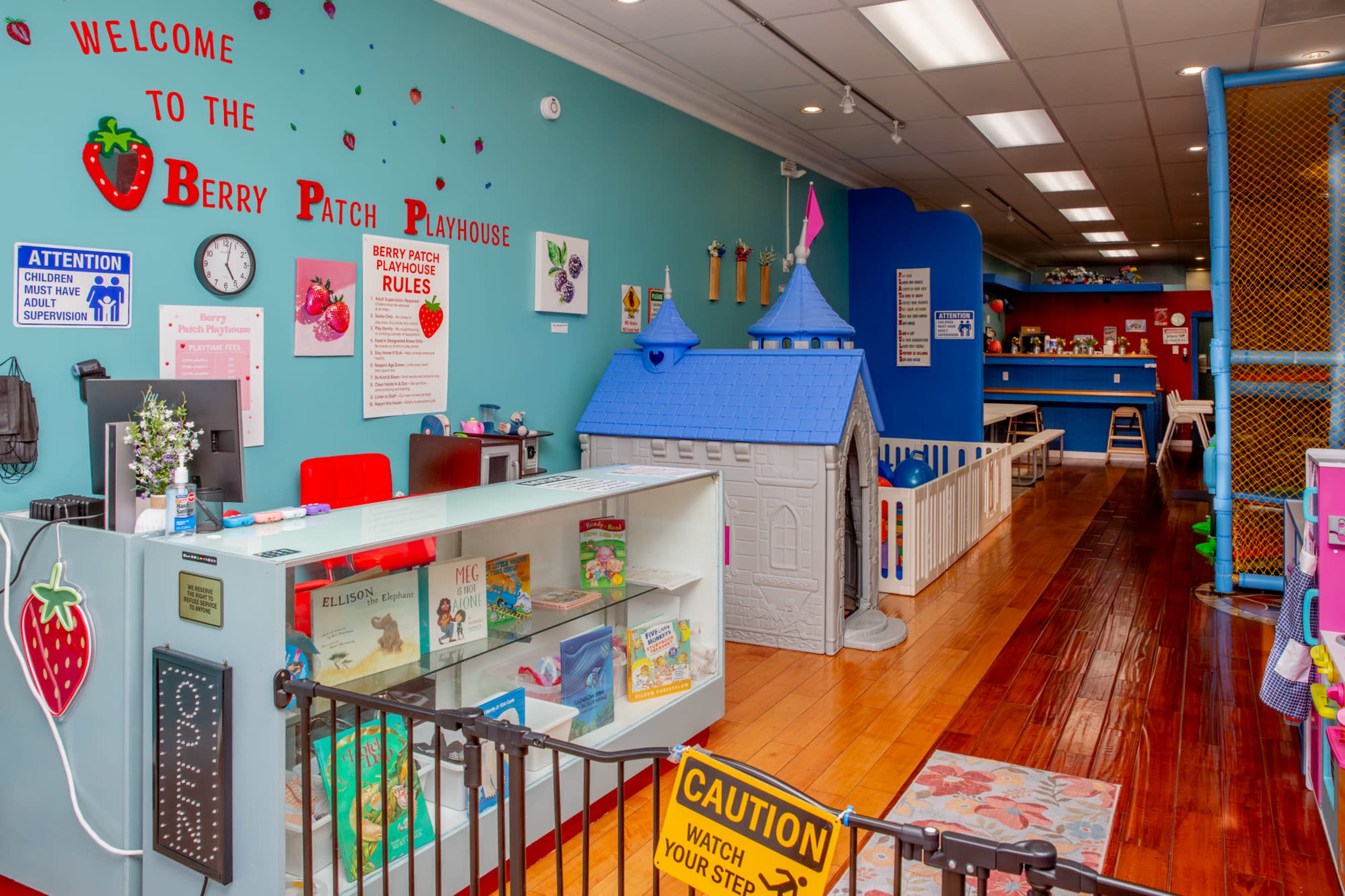 The image shows a brightly colored playroom named "Berry Patch Playhouse," featuring a reception area with a small counter, toys on display, and a play structure in the background.