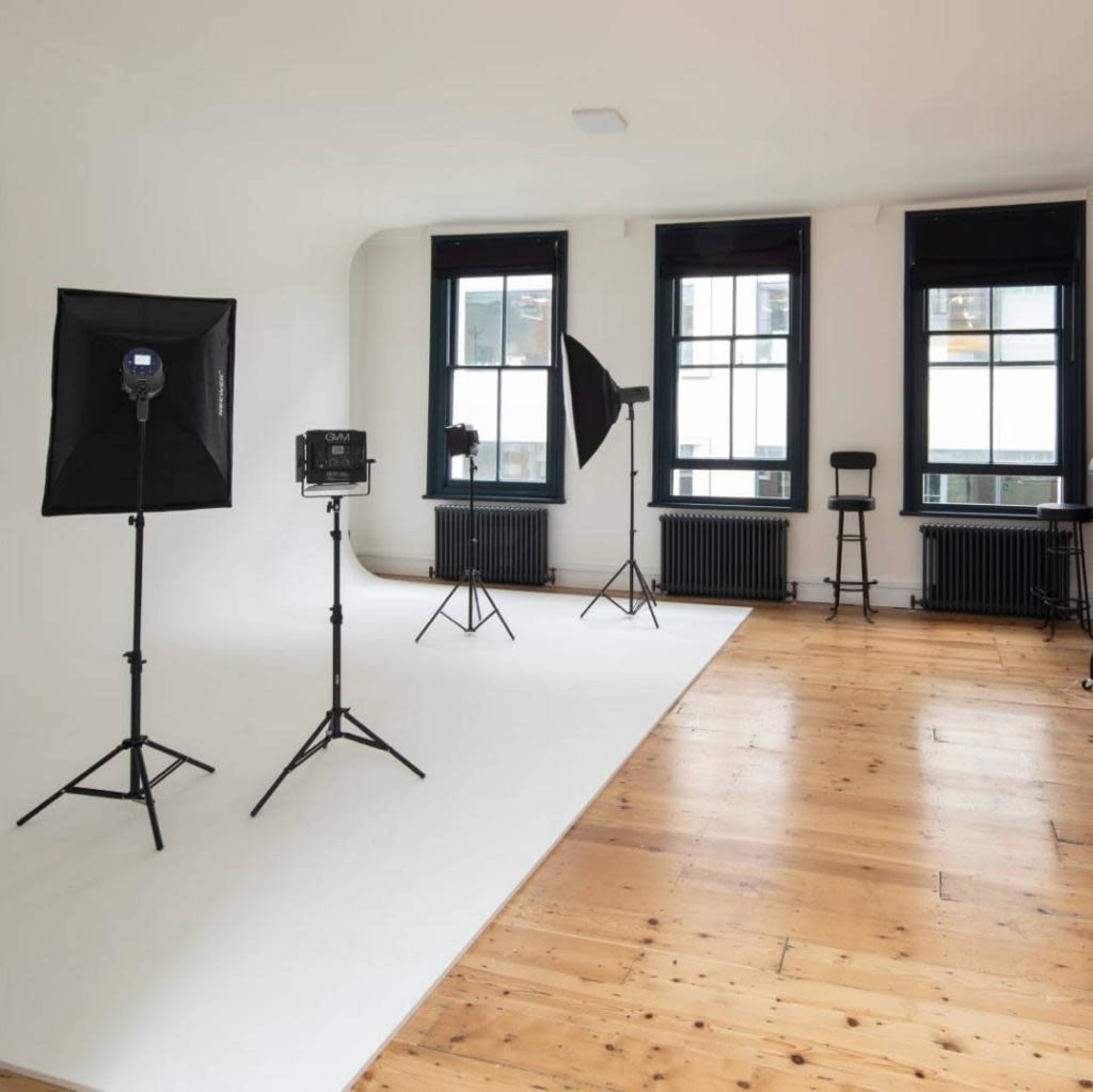 A photography studio with three lighting setups and large windows overlooking a minimalist wooden floor.