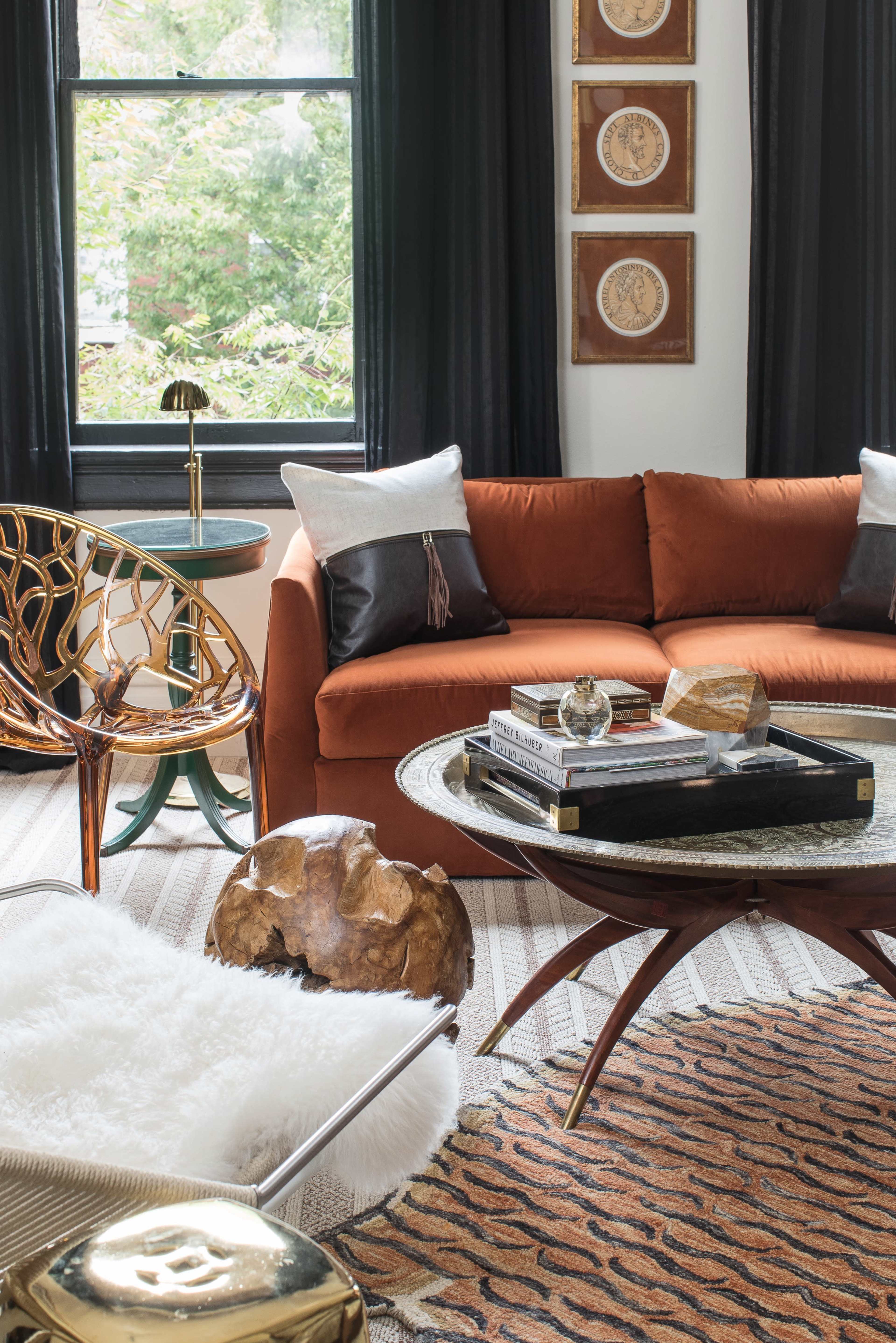 The image features a cozy living room with an orange sofa, a round coffee table, decorative pillows, a rug, and unique accent chairs.