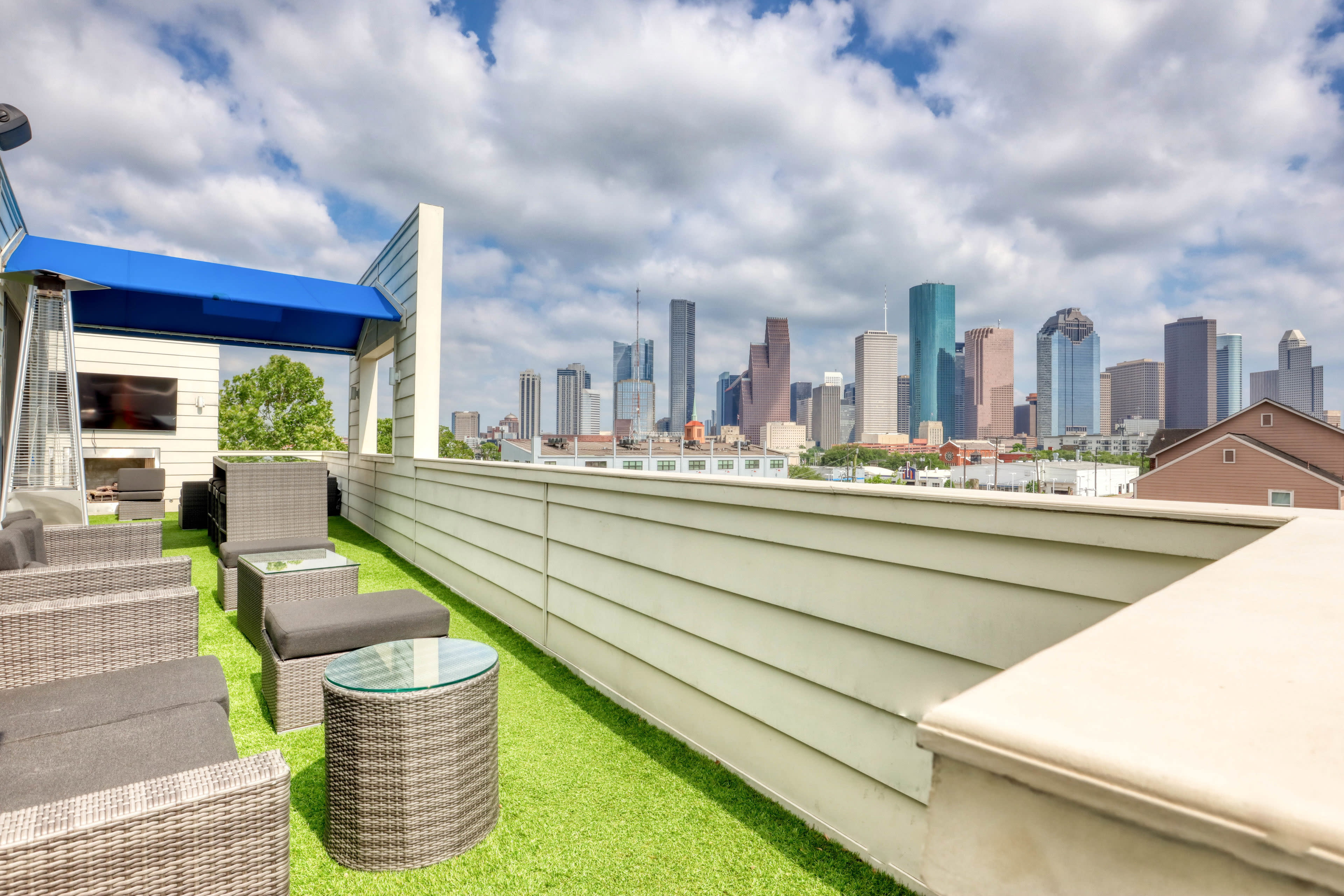 A rooftop terrace with lounge seating and a clear view of the Houston skyline under a partly cloudy sky.