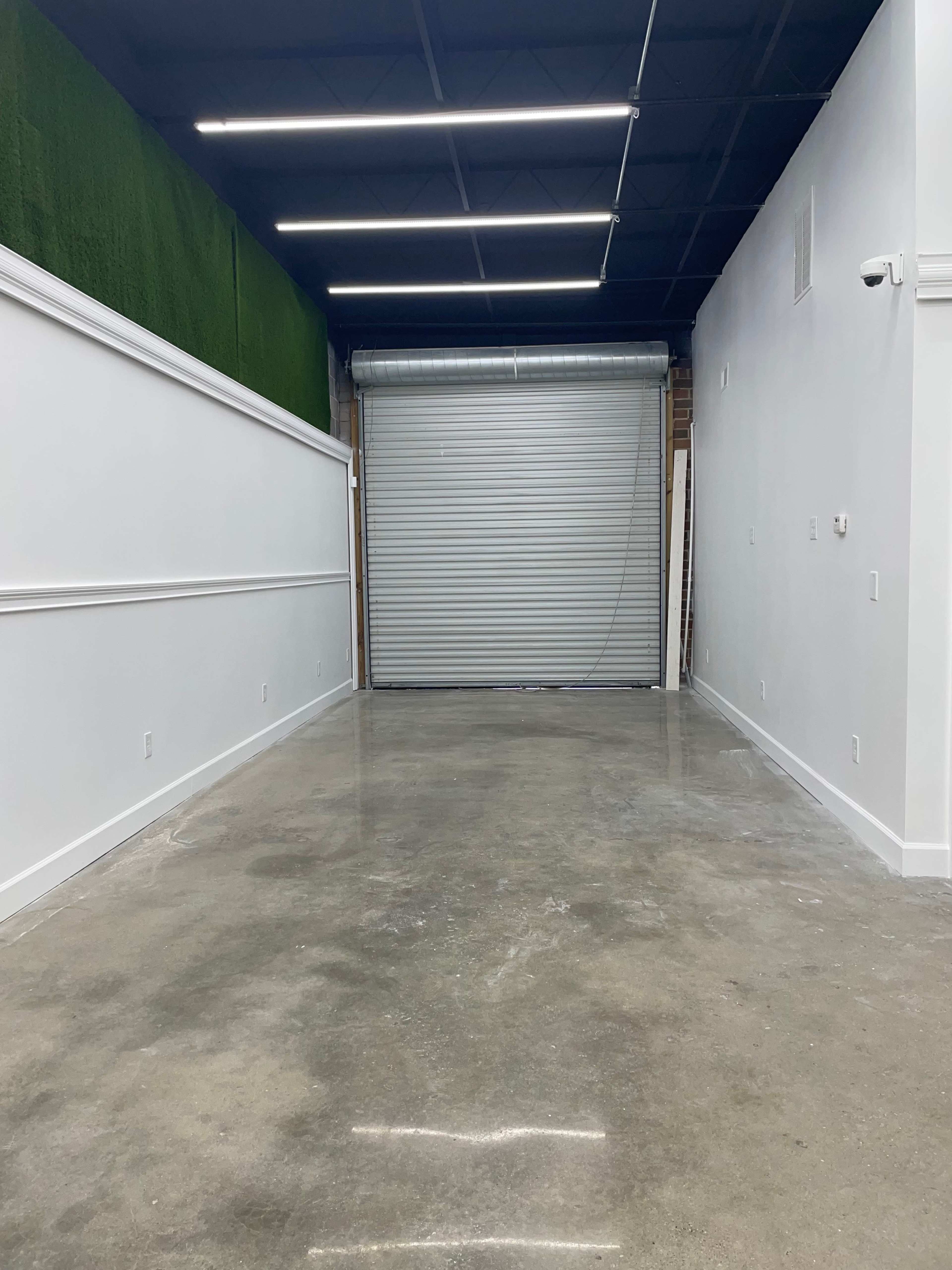 A spacious, empty interior with polished concrete floors and a large closed roll-up door at the far end.