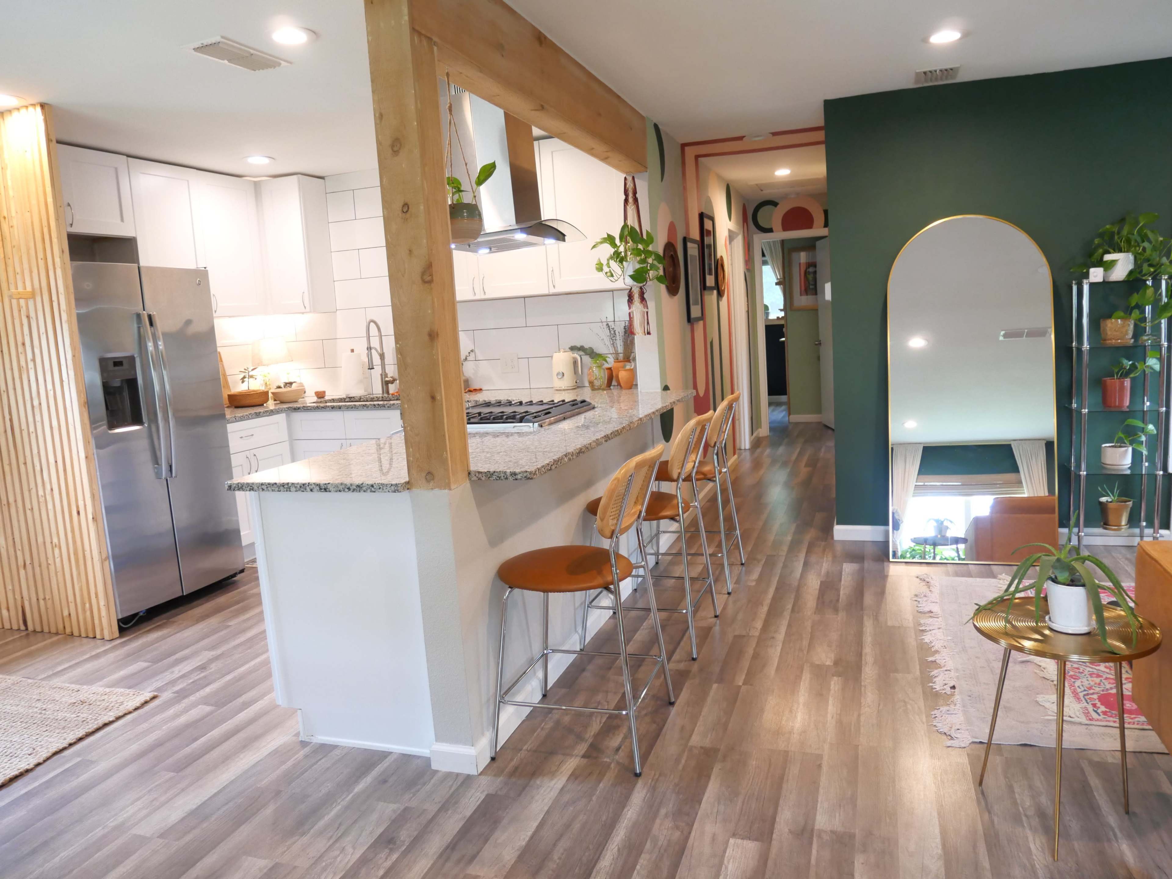 A modern kitchen with a breakfast bar and stools, leading into a hallway that opens to a living area with plants and decorative elements.