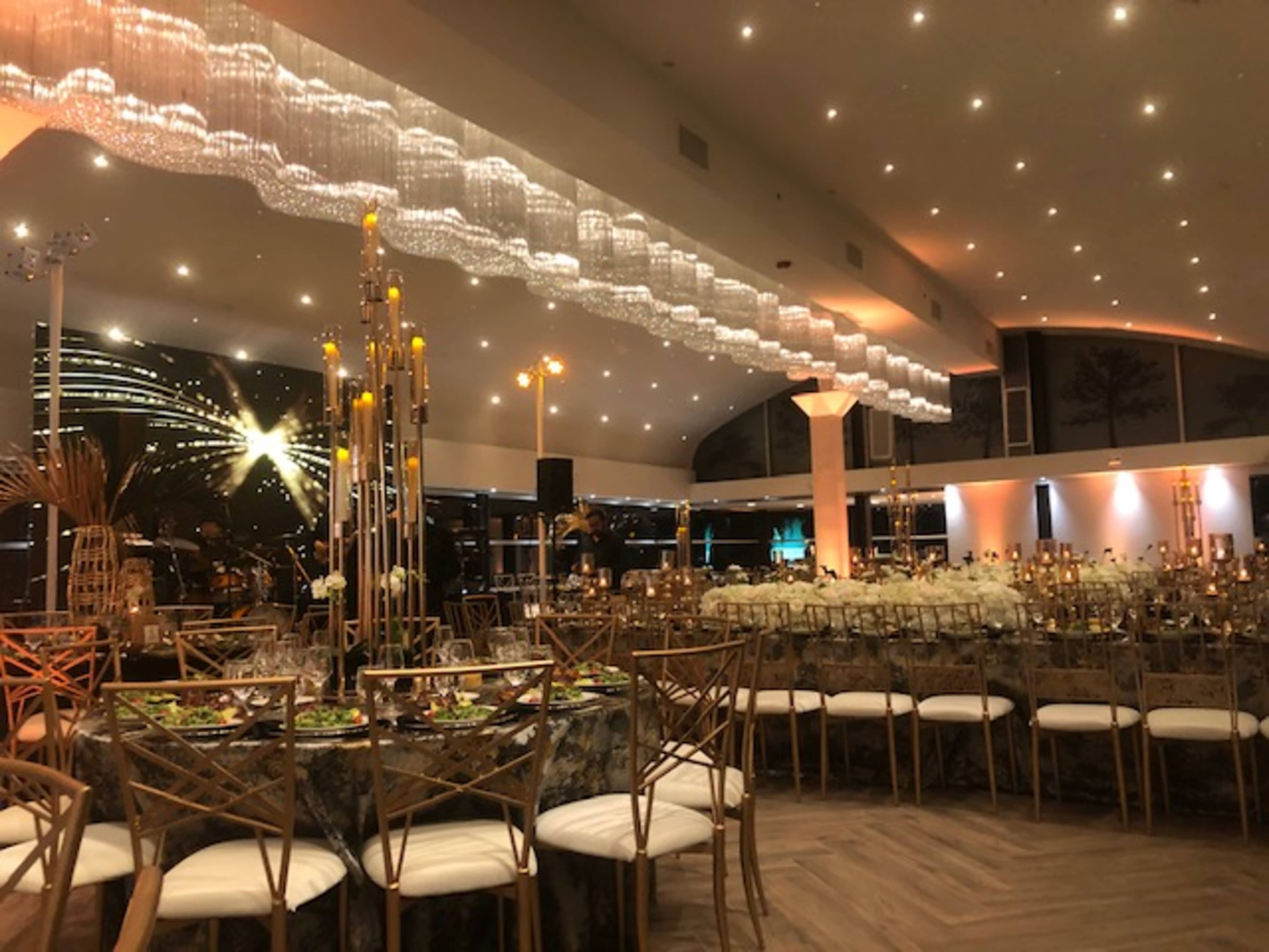 An elegantly arranged dining area with tables set for an event, featuring chandeliers and candlelight in a spacious venue.