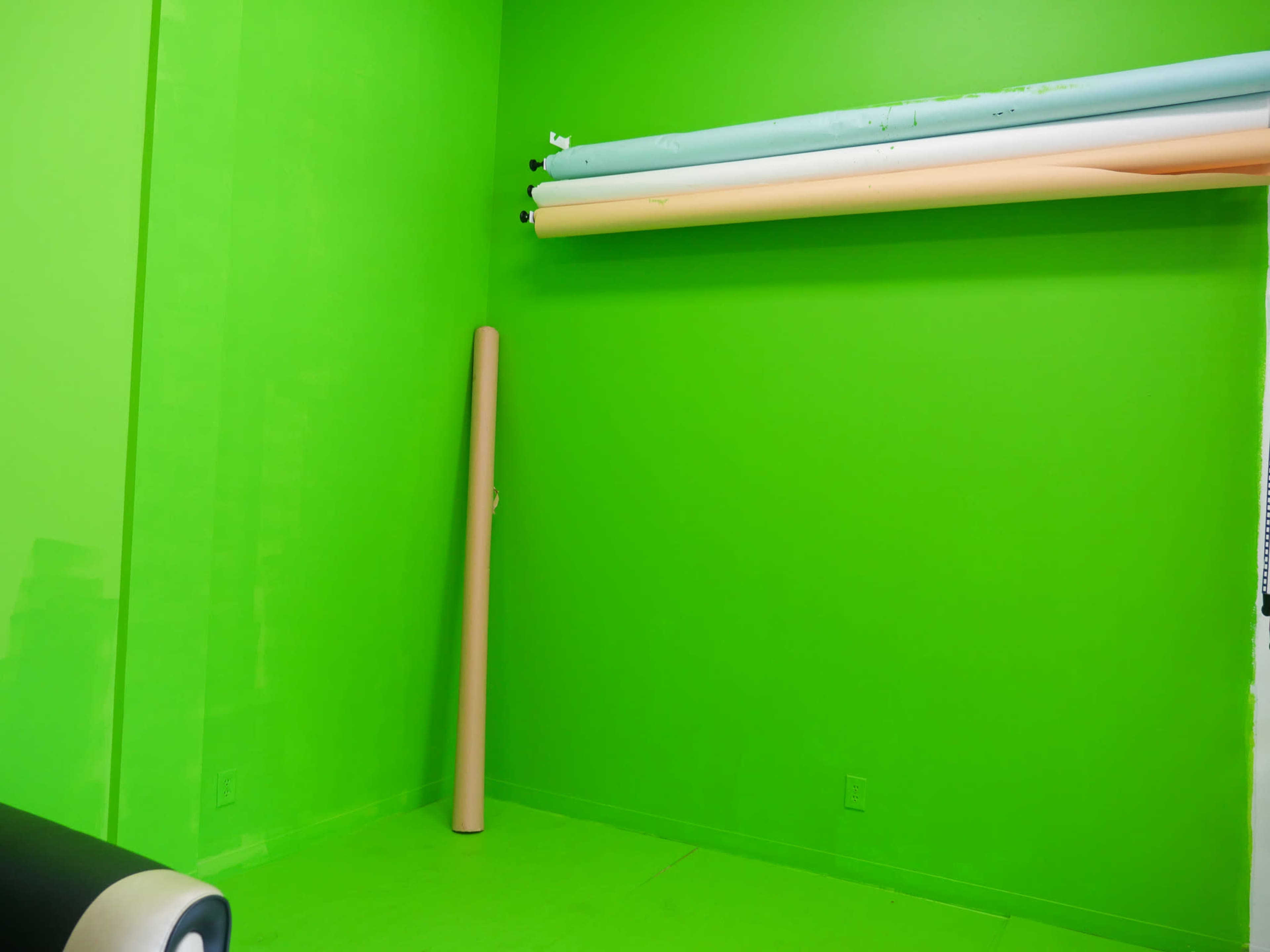 The image shows a bright green room with several rolls of colored backdrop paper stored on a shelf.