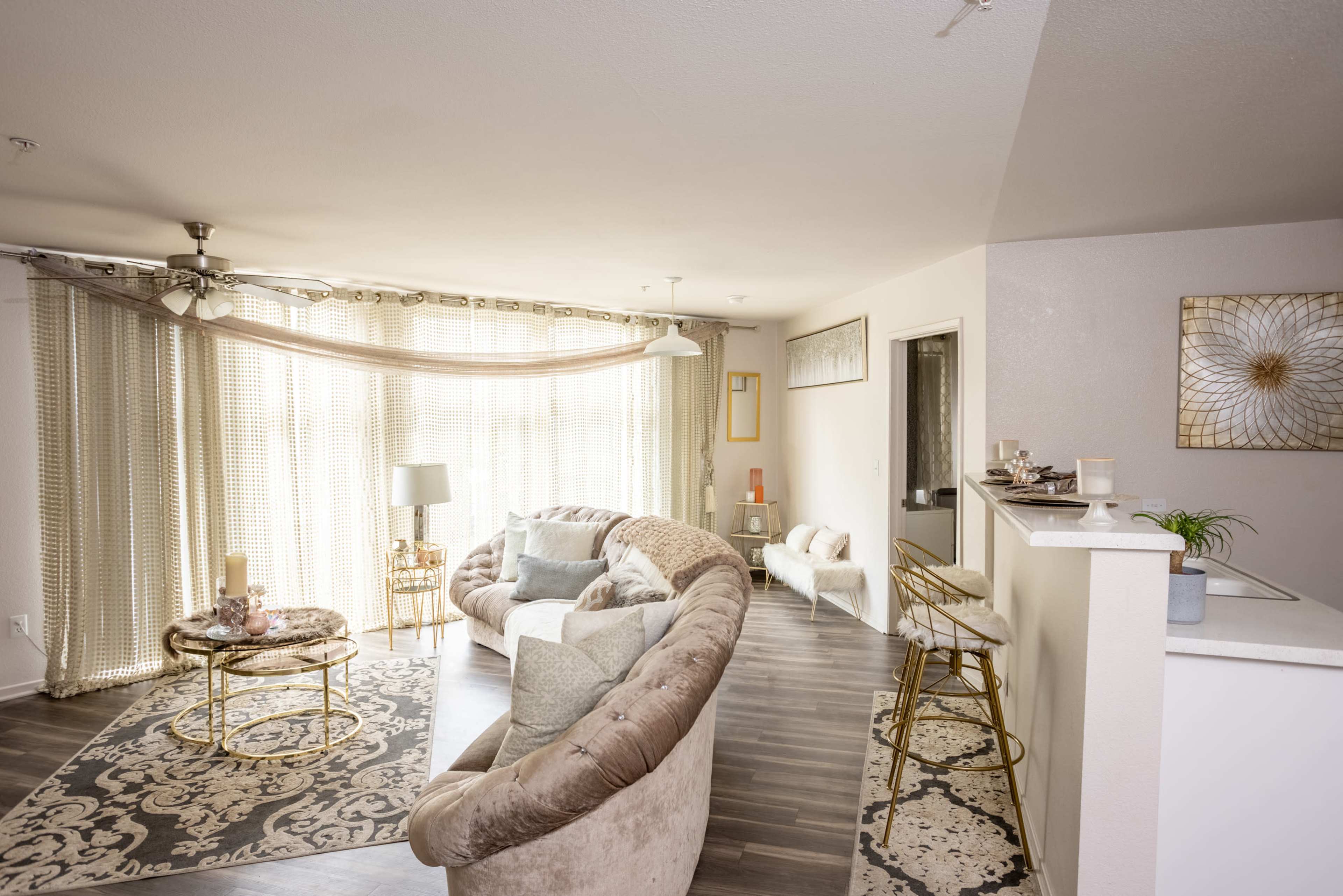 A modern living room with a curved sofa, decorative pillows, a round coffee table, and a kitchen counter visible in the background.