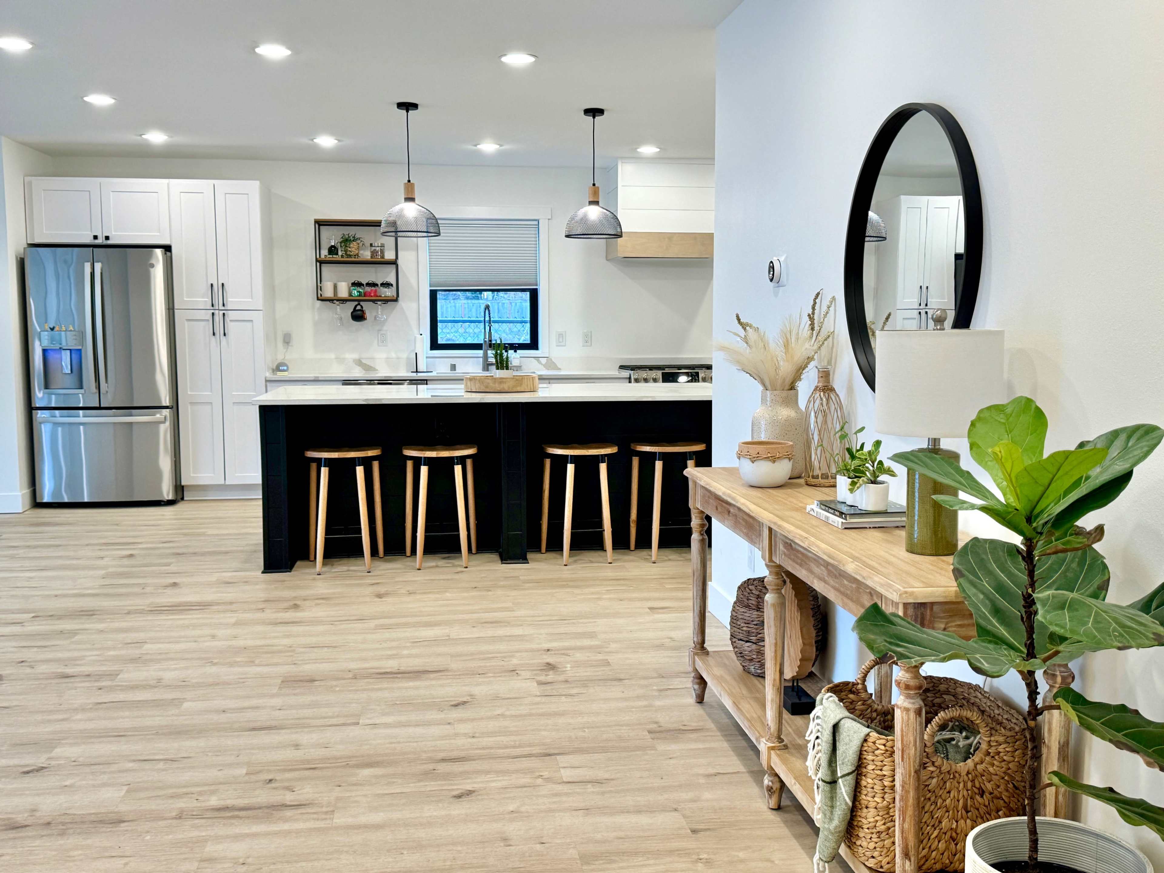 A modern kitchen and dining area features a white countertop, black island with stools, stainless steel appliances, and light wood flooring.