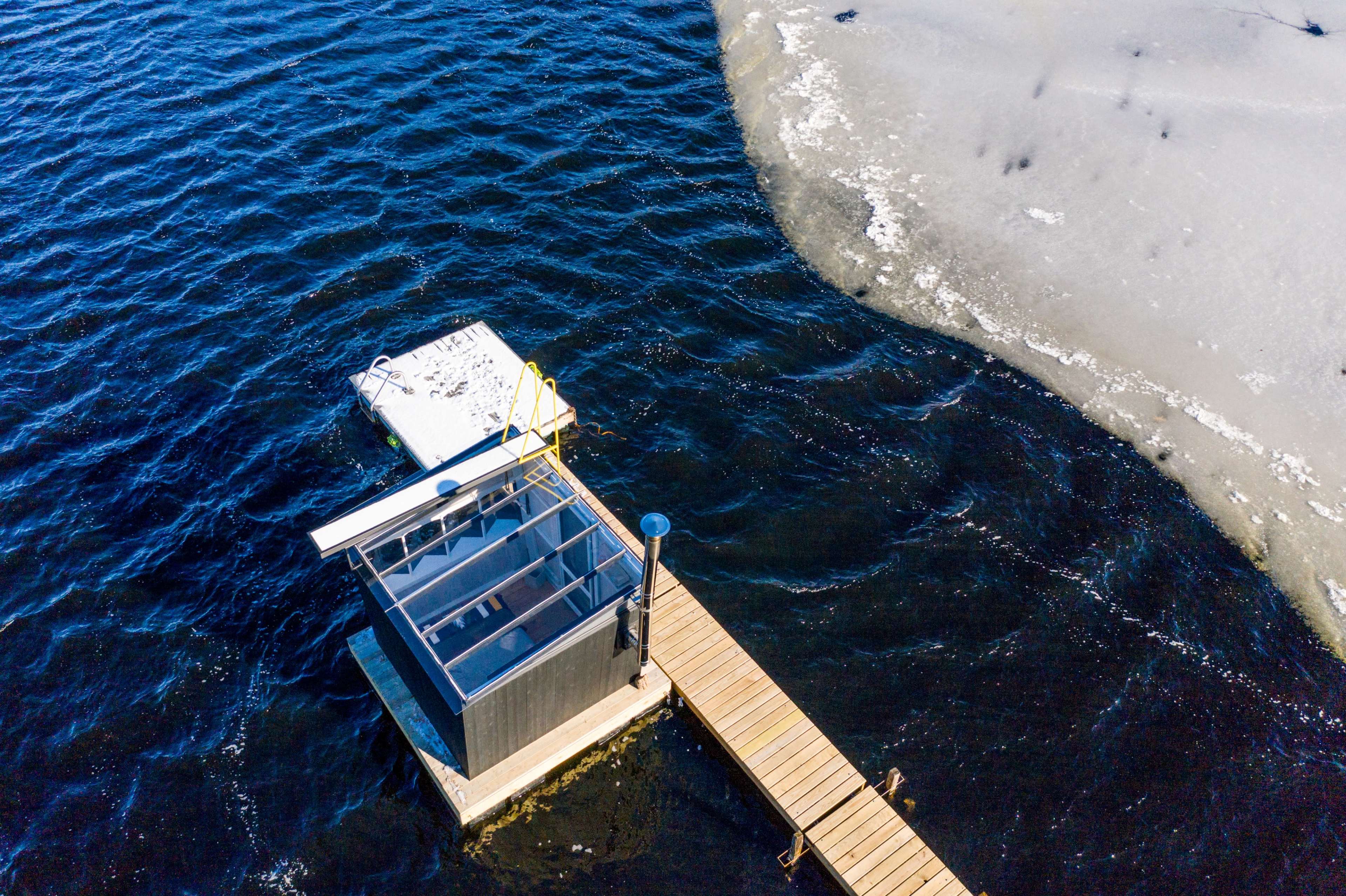 A wooden dock extends over dark water, with a small enclosed structure at its end and patches of ice visible nearby.