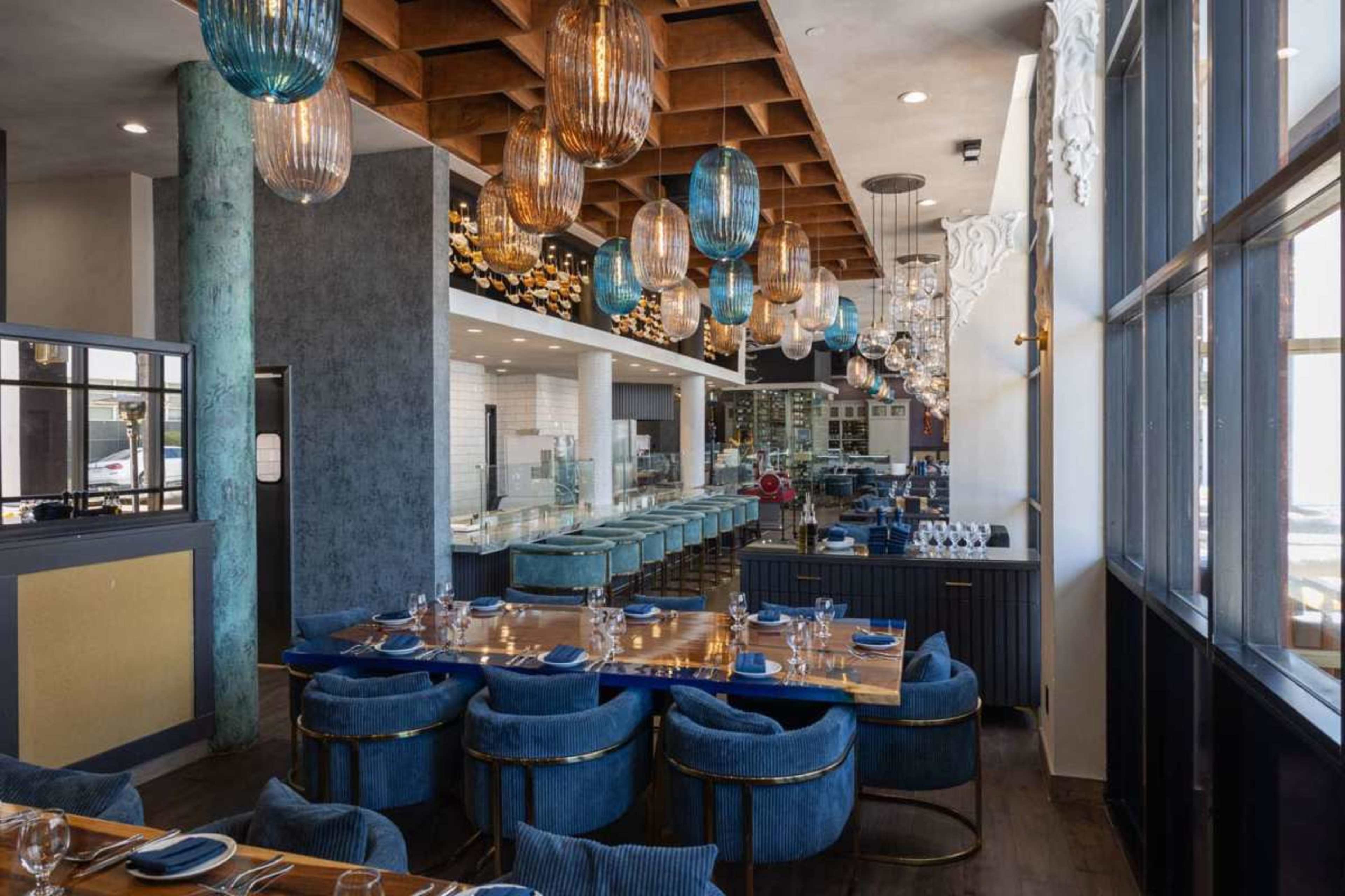 The image shows a modern restaurant interior with blue upholstered seating, wooden tables, and decorative pendant lighting hanging from the ceiling.