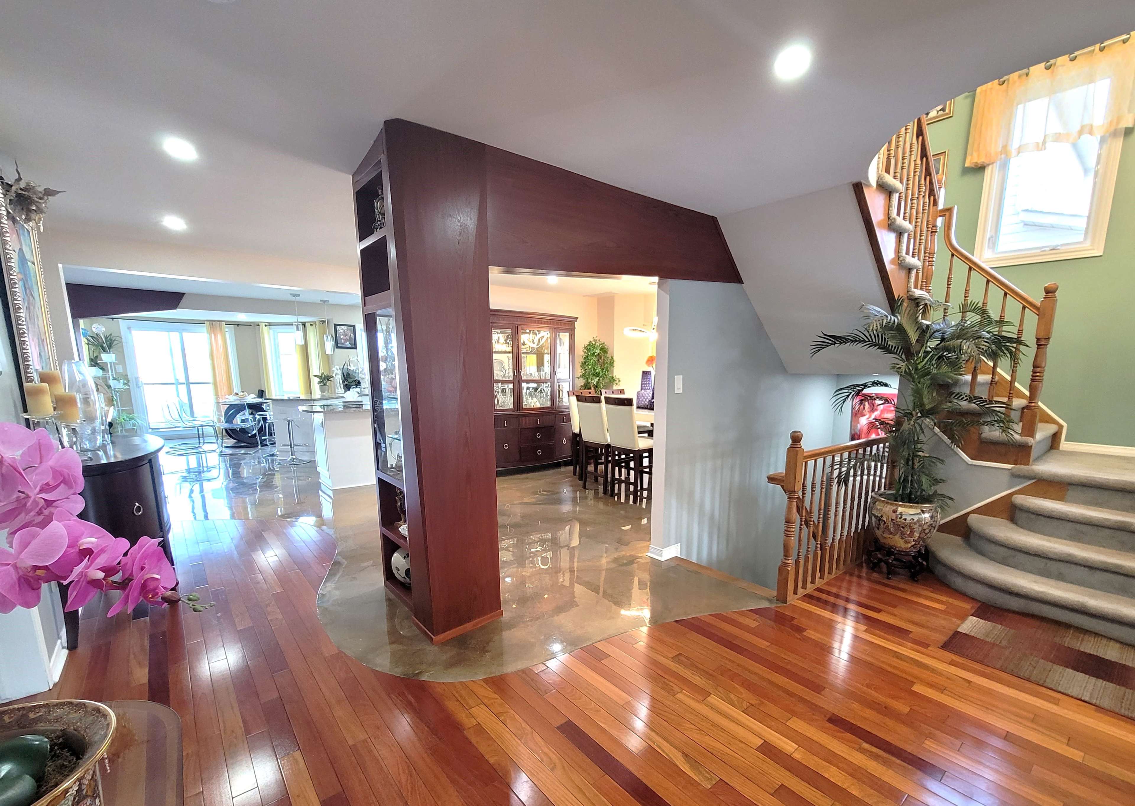 A well-lit foyer with polished wooden floors, a staircase on the right, and a view of a dining area through an archway.