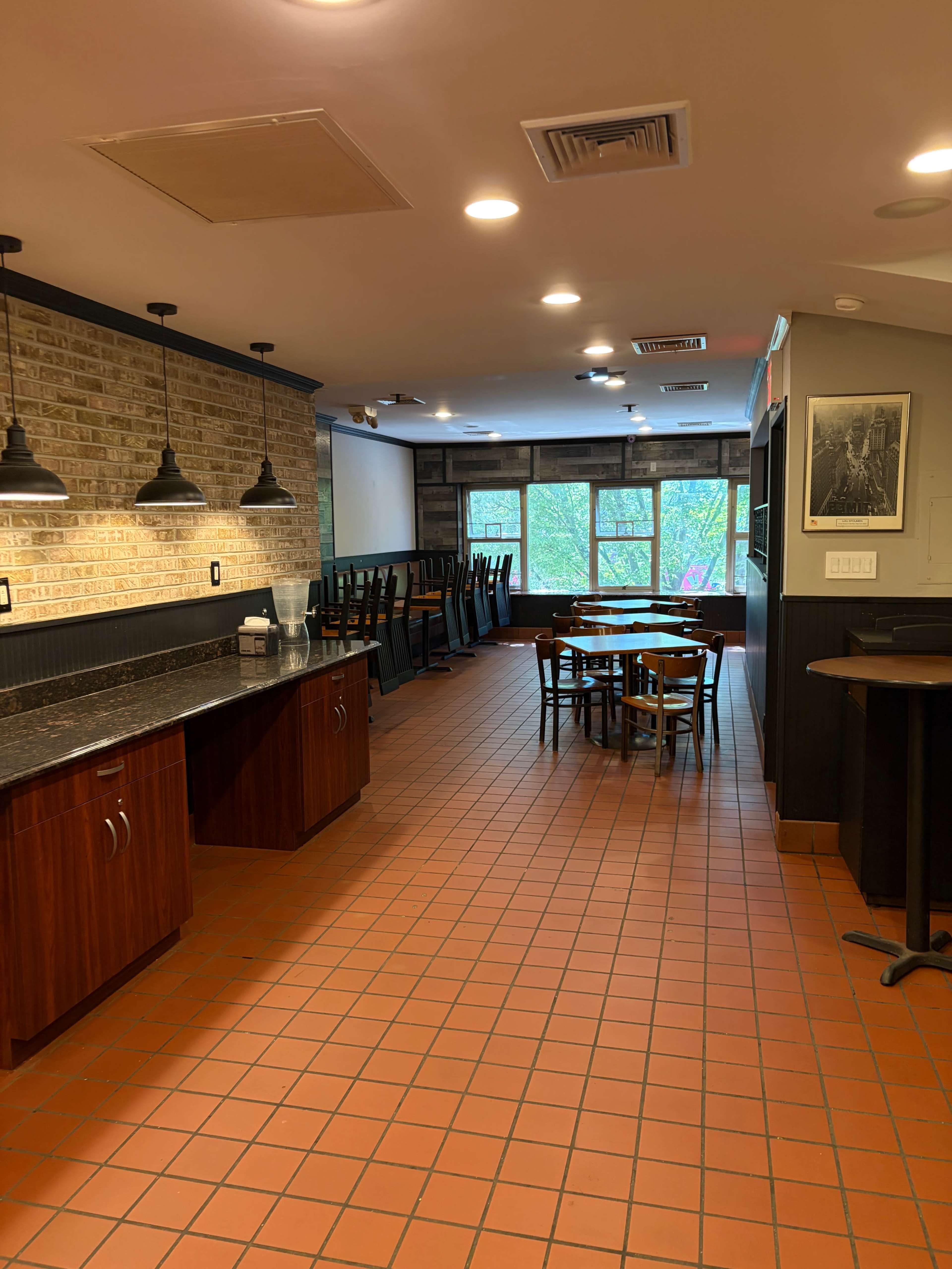 The image shows a restaurant interior with stacked chairs on tables, brick walls, and a tiled floor.