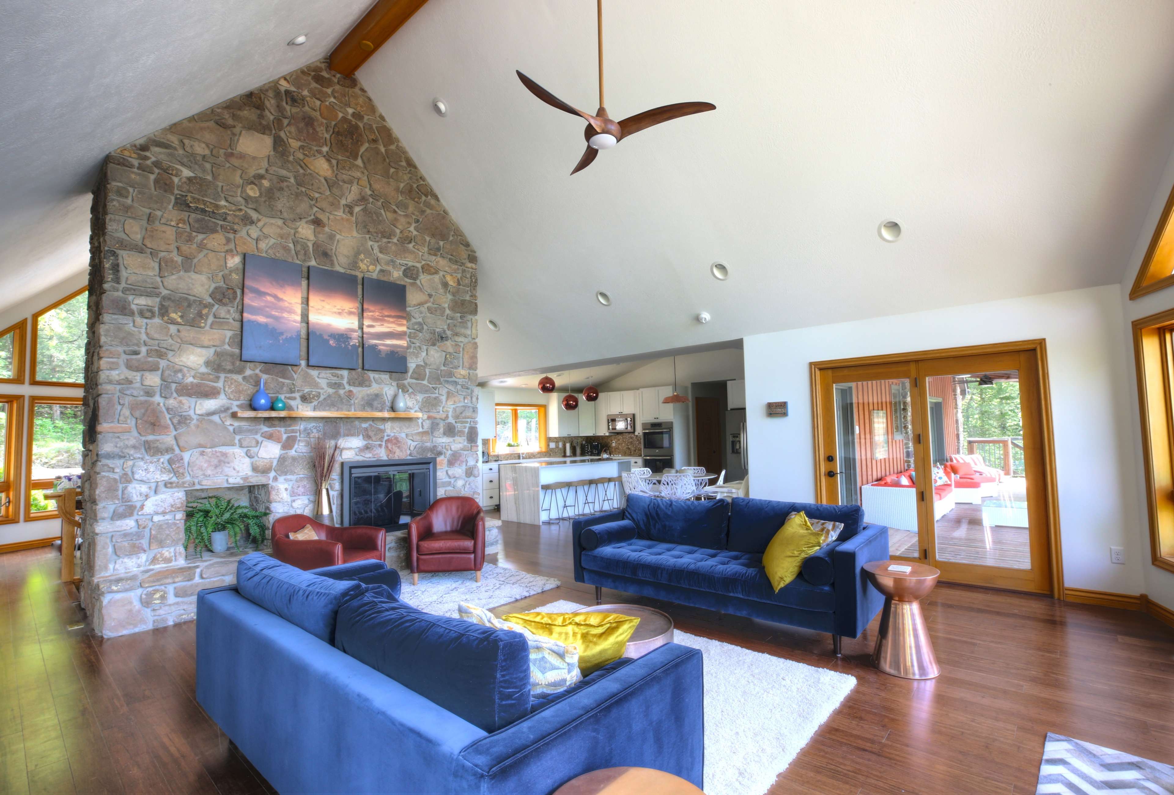 A spacious living room featuring a stone fireplace, two blue sofas, and a dining area in the background with large windows.