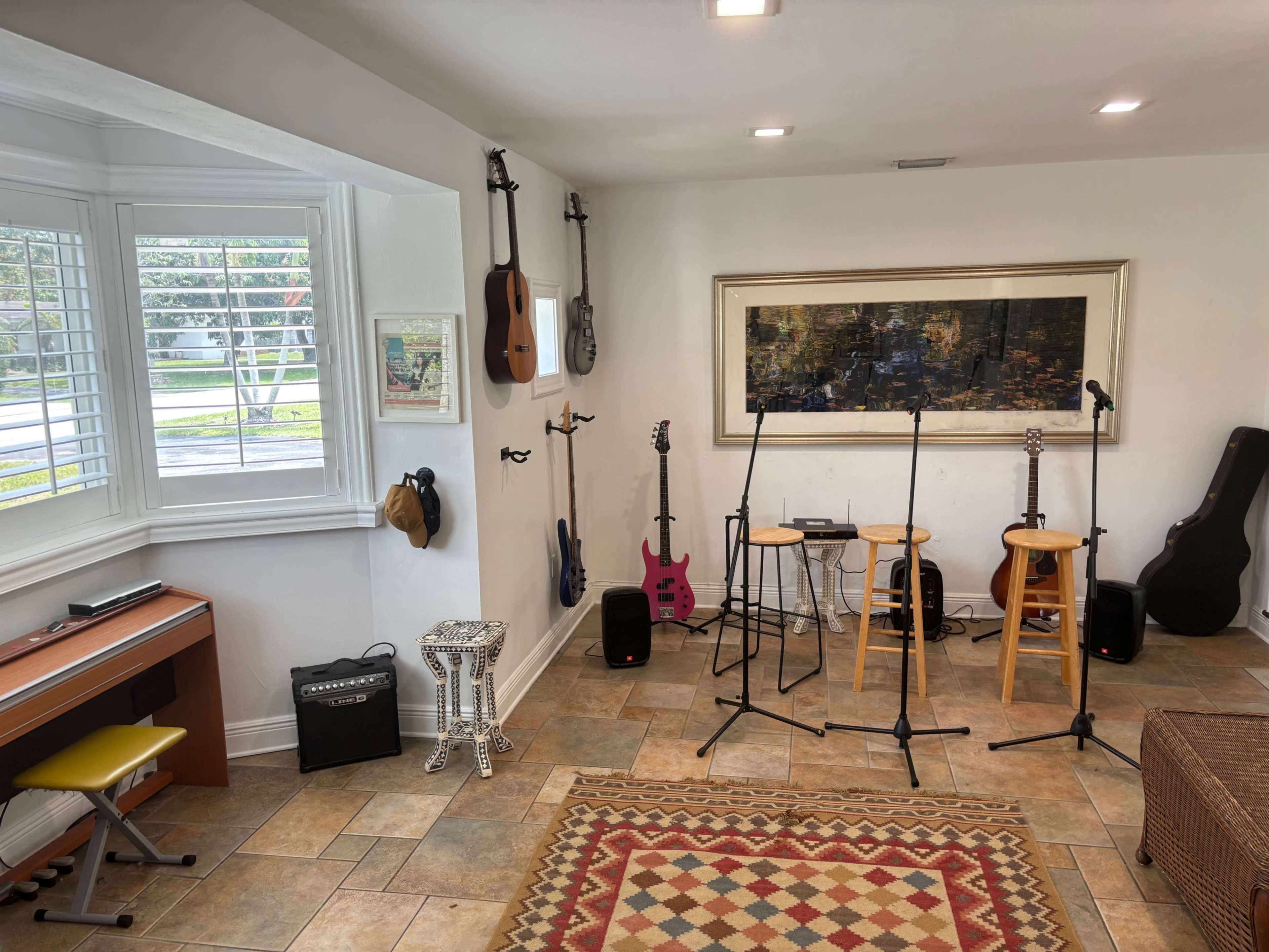 A cozy music room featuring various musical instruments, two tall stools, and standing microphone stands against a light-colored wall.