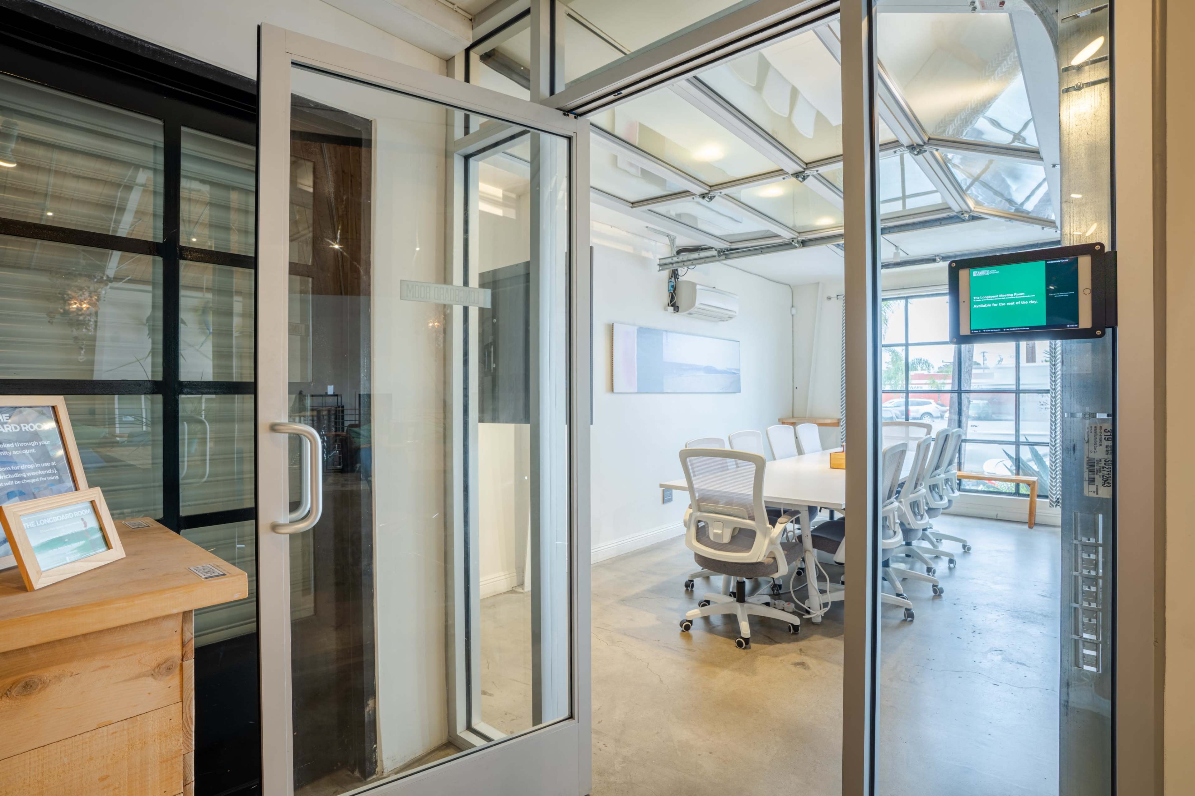 The image shows a modern conference room with a glass ceiling and large windows, featuring a long white table surrounded by ergonomic chairs.