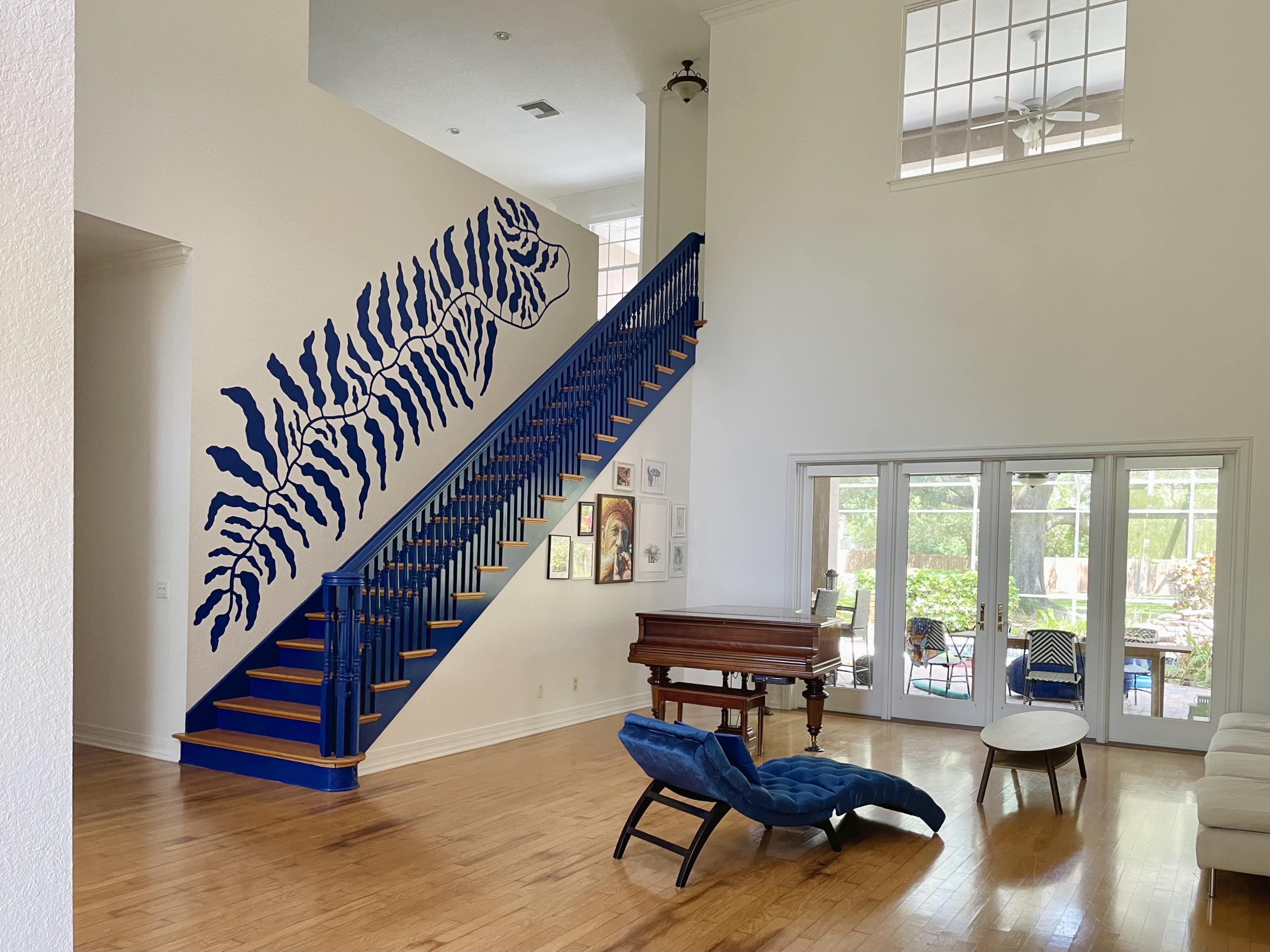 A staircase with blue railings and a large zebra mural ascends to a second floor in a bright living space featuring hardwood floors and large windows.