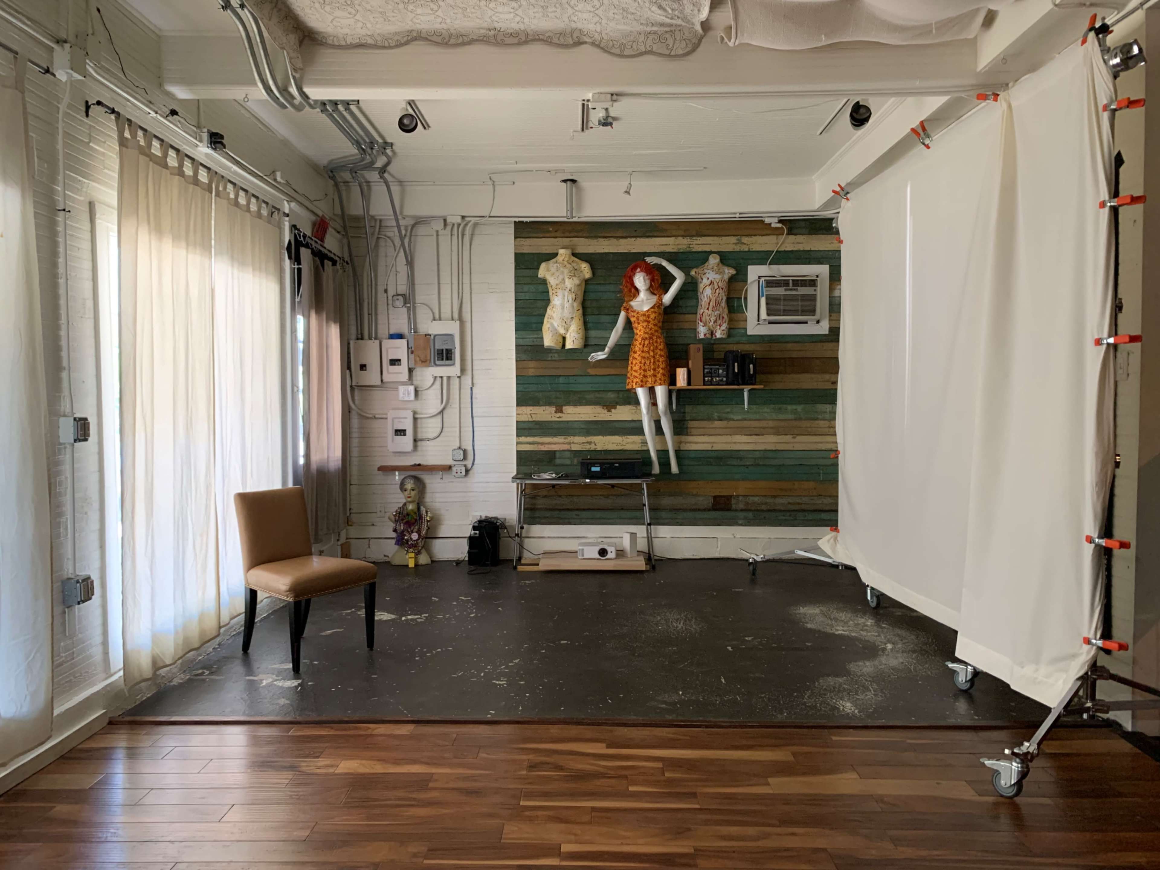 The image shows a well-lit studio space featuring a wooden accent wall, a chair, a projector on the floor, and two mannequins dressed in clothing.
