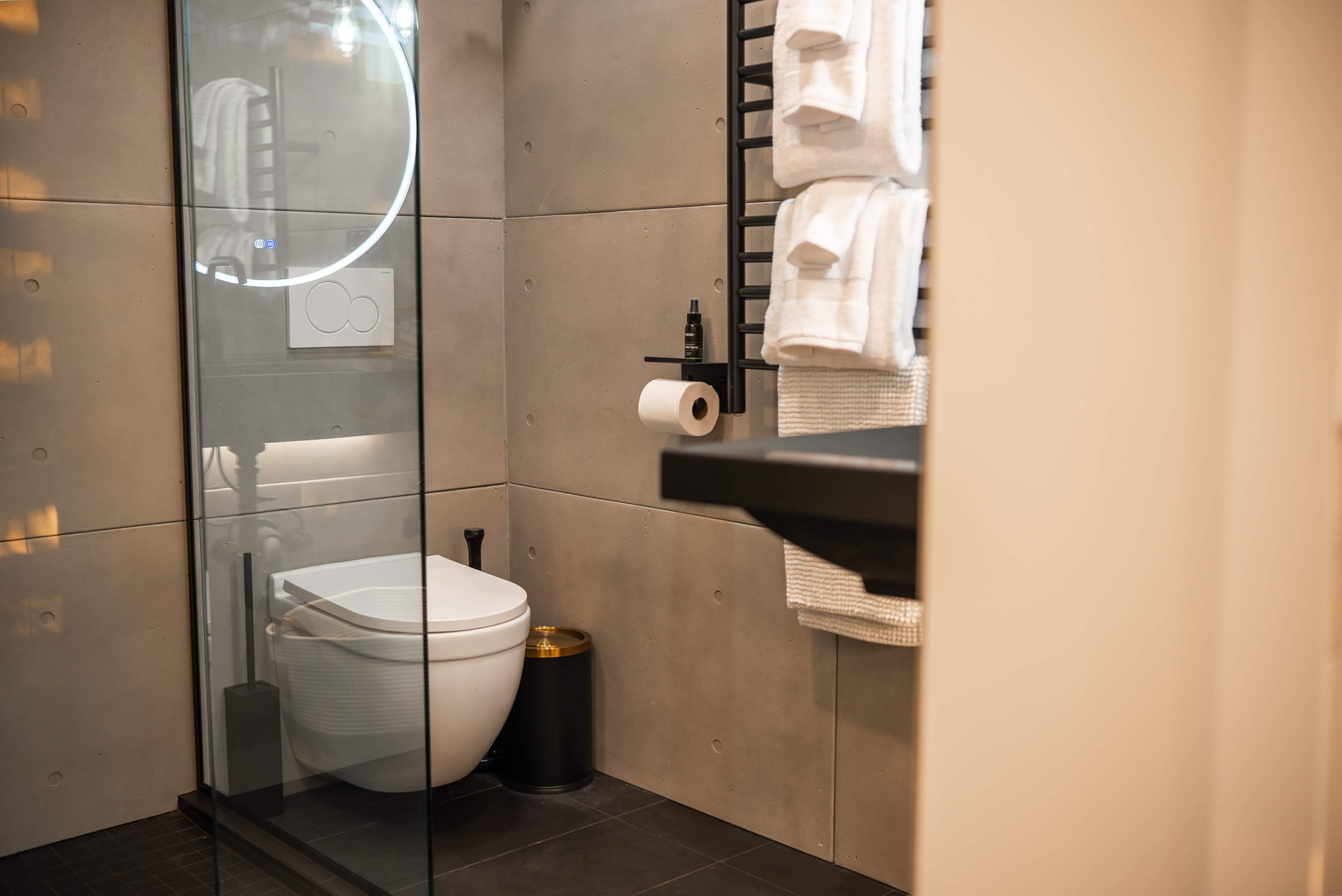 The image shows a modern bathroom featuring a glass shower, a white toilet, and neatly arranged towels.