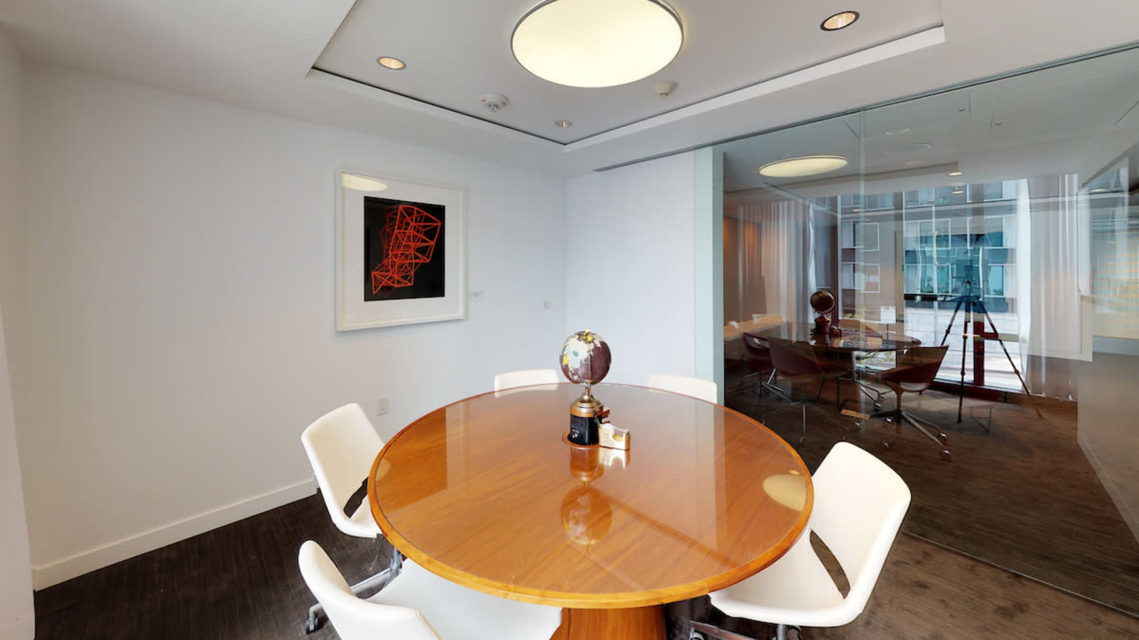A modern conference room with a circular wooden table surrounded by white chairs and a globe on a pedestal.