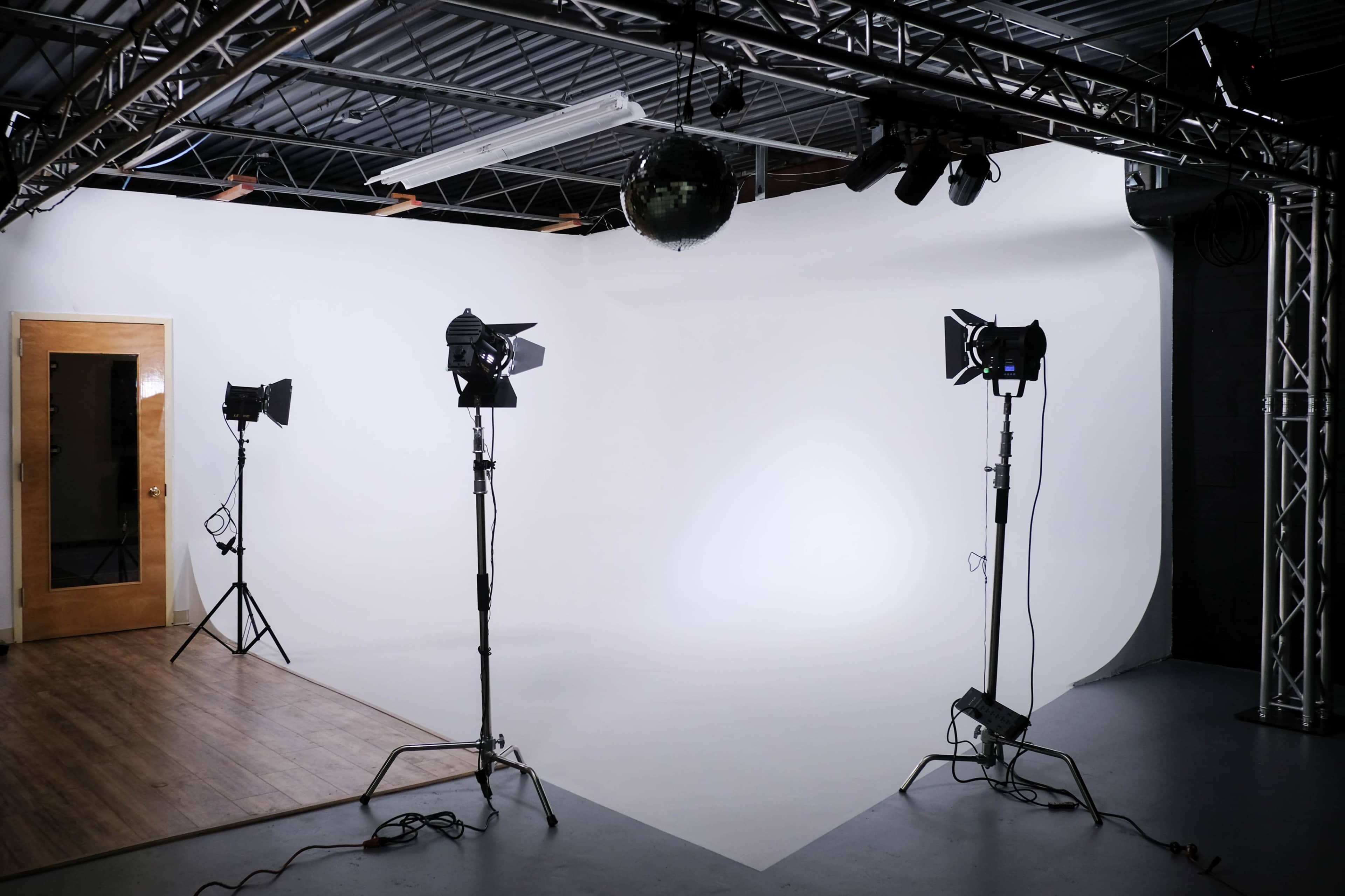 The image shows a photography studio with a white backdrop, three lighting setups, and a mirror ball hanging from the ceiling.