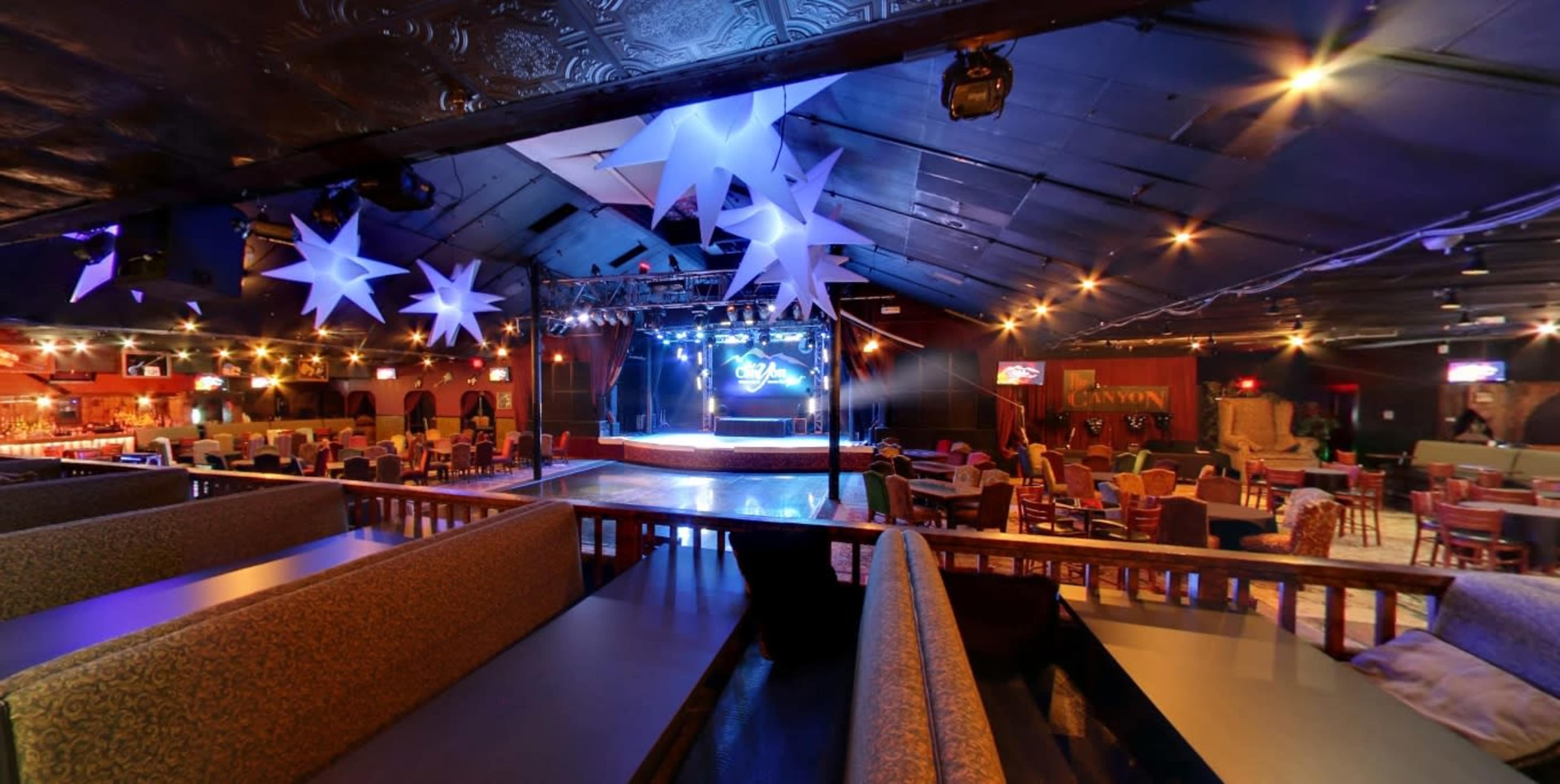 An empty event space with a stage at the front, decorated with star-shaped hanging ornaments and surrounded by seating areas.