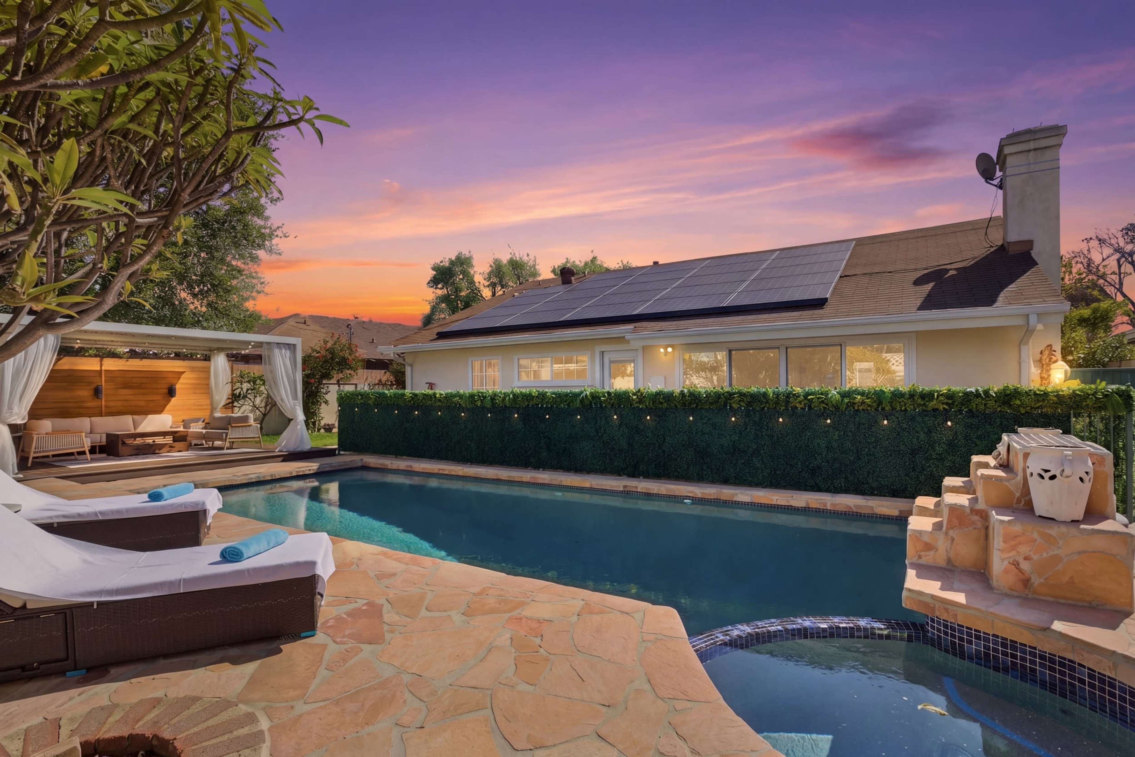 The image shows a backyard pool area with lounge chairs, a spa, and a house with solar panels under a colorful sunset sky.