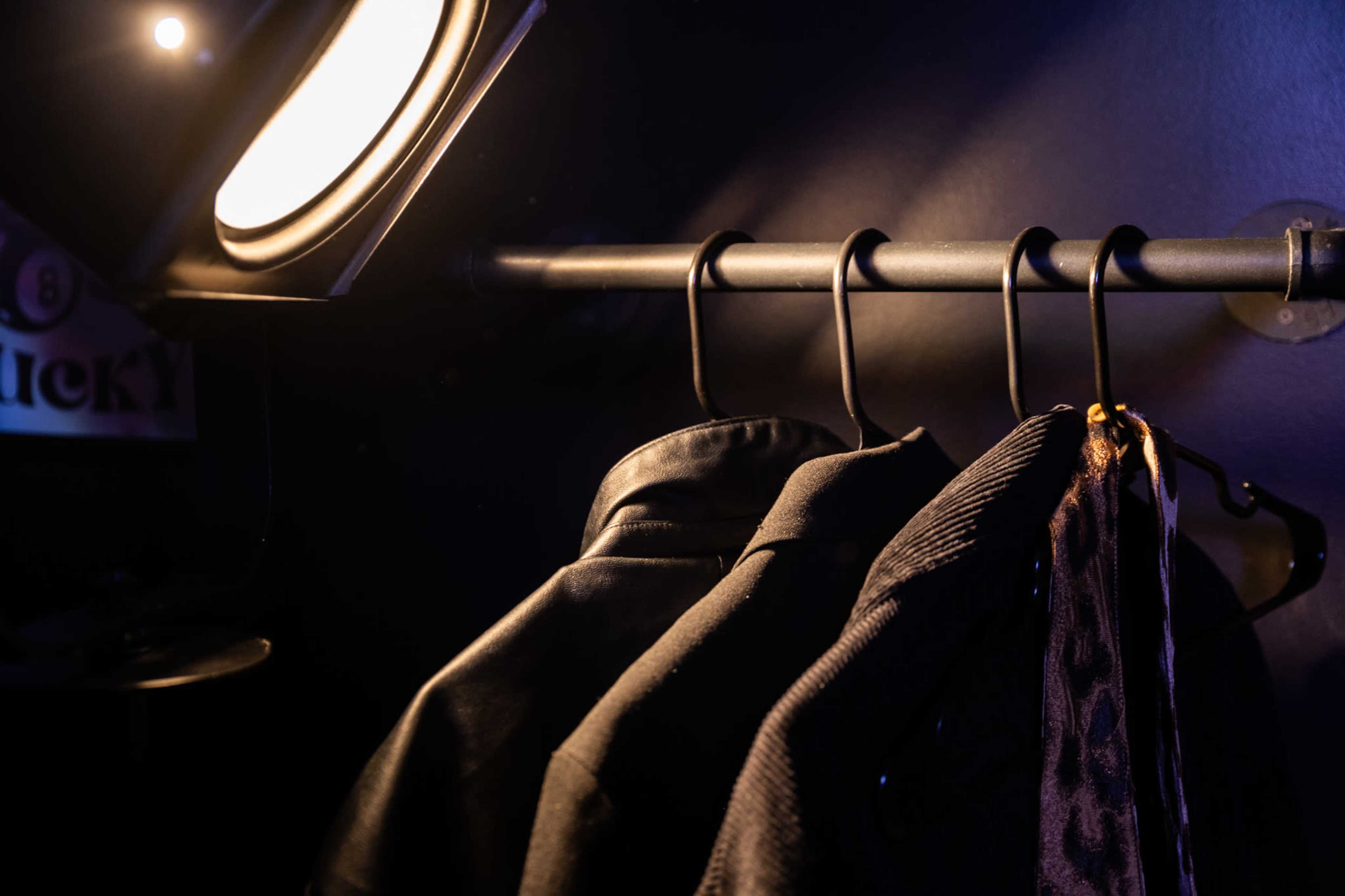 Three jackets hang on a rack under a spotlight against a dark wall.