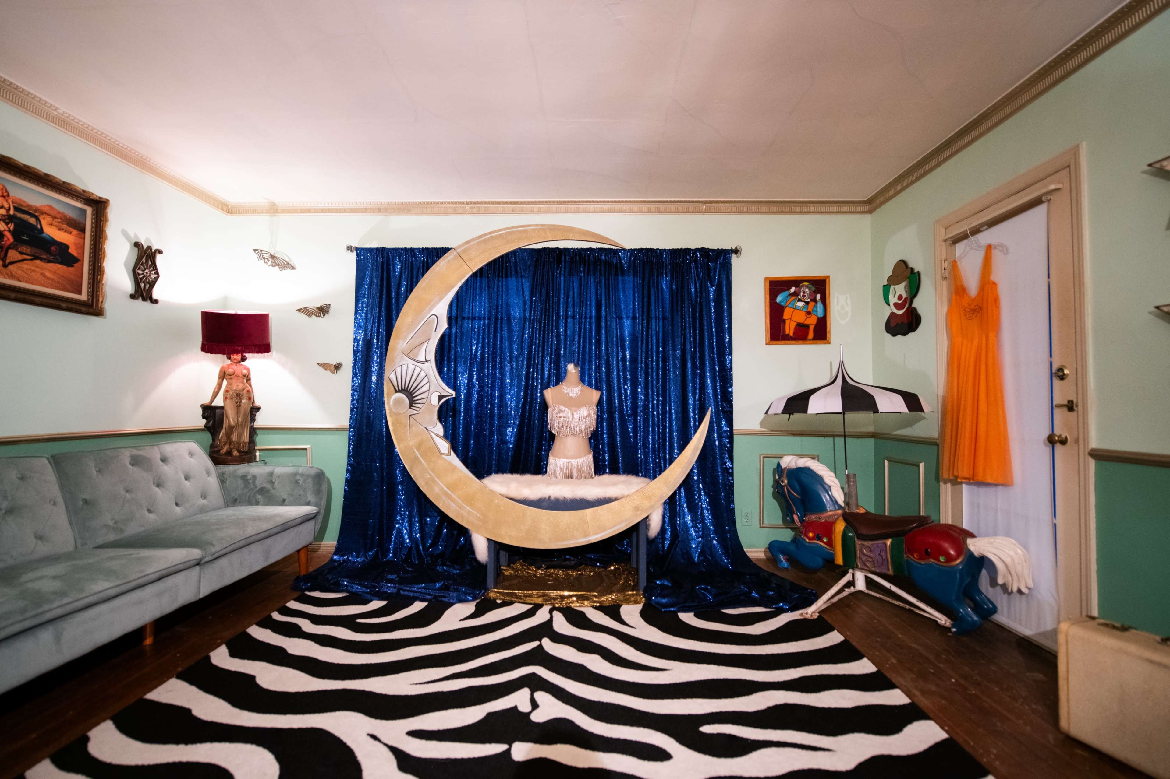 The image shows a whimsical room with a crescent moon backdrop, a mannequin in front of it, a patterned rug, and various decorations on the walls.