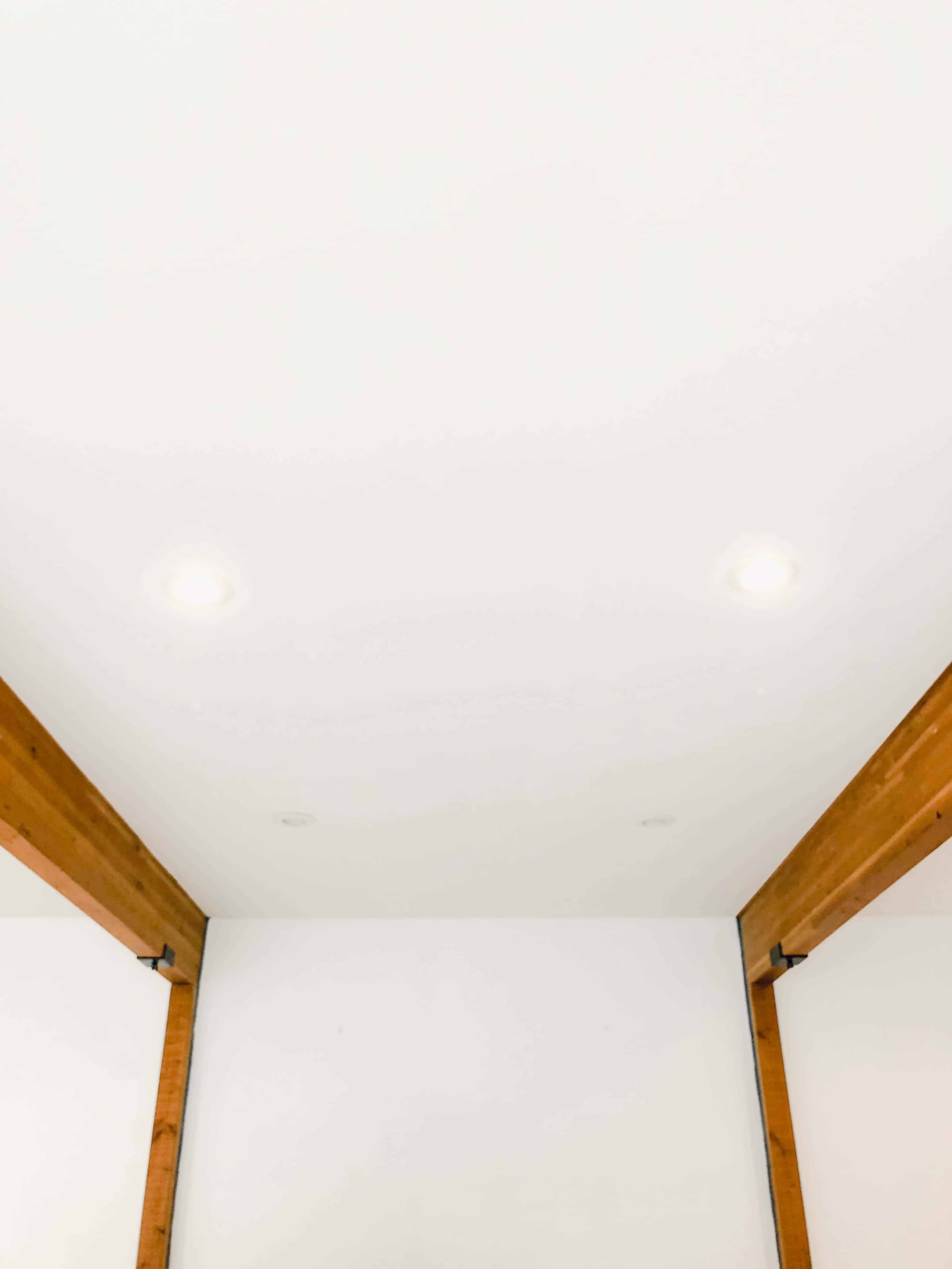 A ceiling with recessed lights and exposed wooden beams in a plain white room.