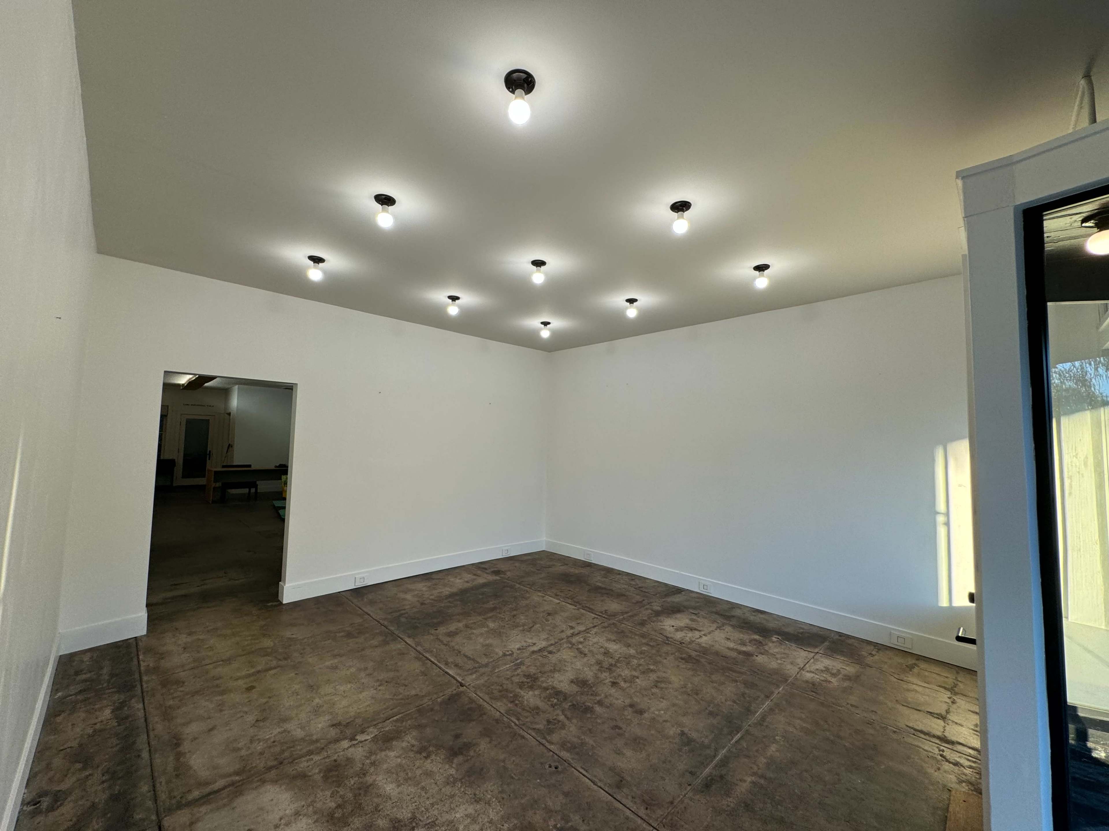 The image shows an empty room with a concrete floor and multiple ceiling lights illuminating the white walls.