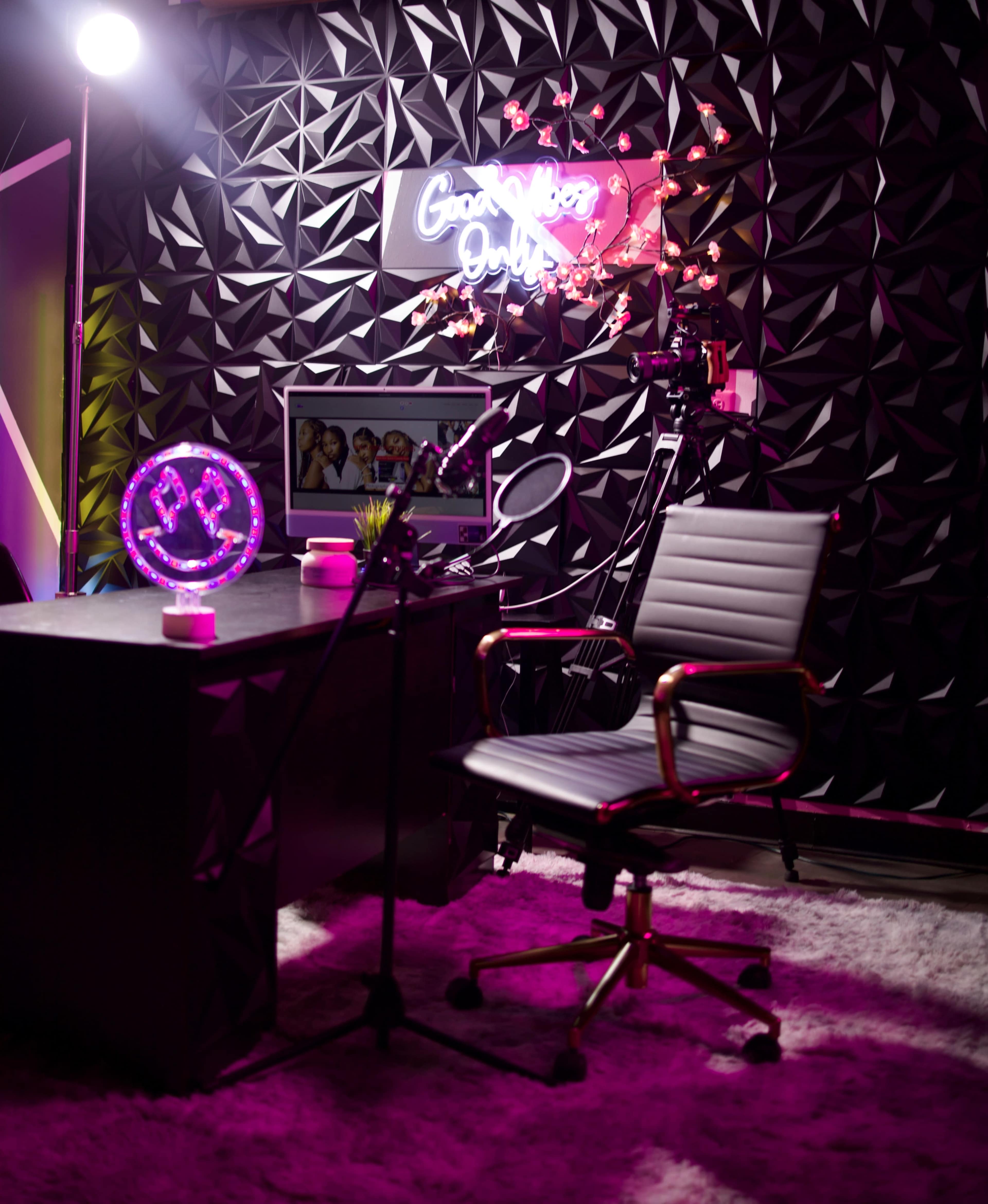 The image shows a modern office space featuring a desk, a swivel chair, a neon sign, and decorative elements like a flower arrangement and a mood lamp.