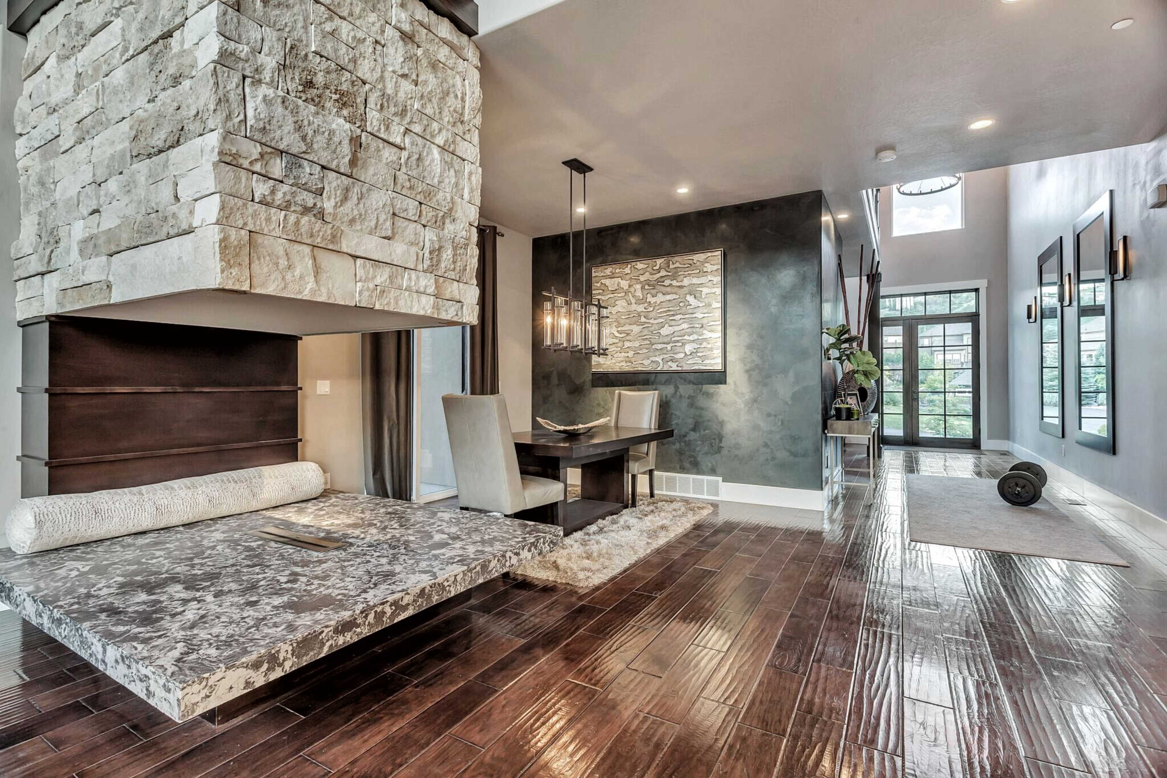 A modern entryway featuring a stone fireplace, a wooden dining table with two chairs, and large windows leading to an outdoor area.