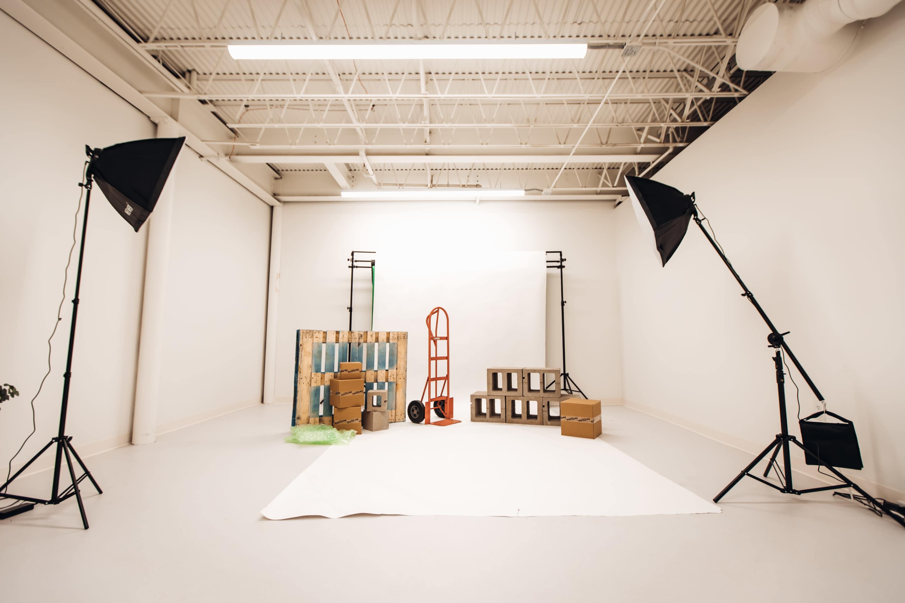 A studio space is arranged with backdrop materials, lighting equipment, and various props including boxes and a dolly.