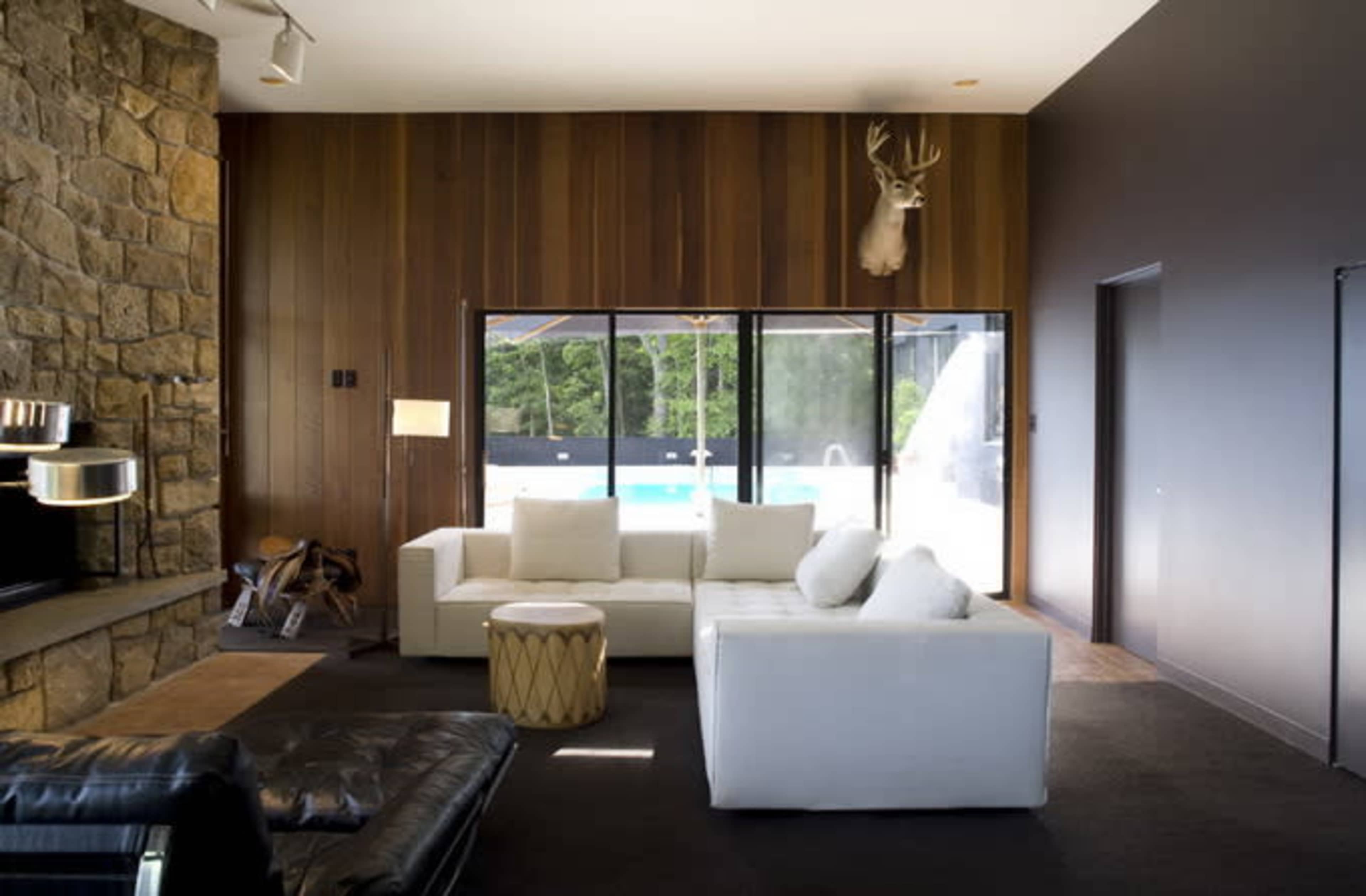 A modern living room with a stone fireplace, a white sectional sofa, and large windows overlooking a pool area.
