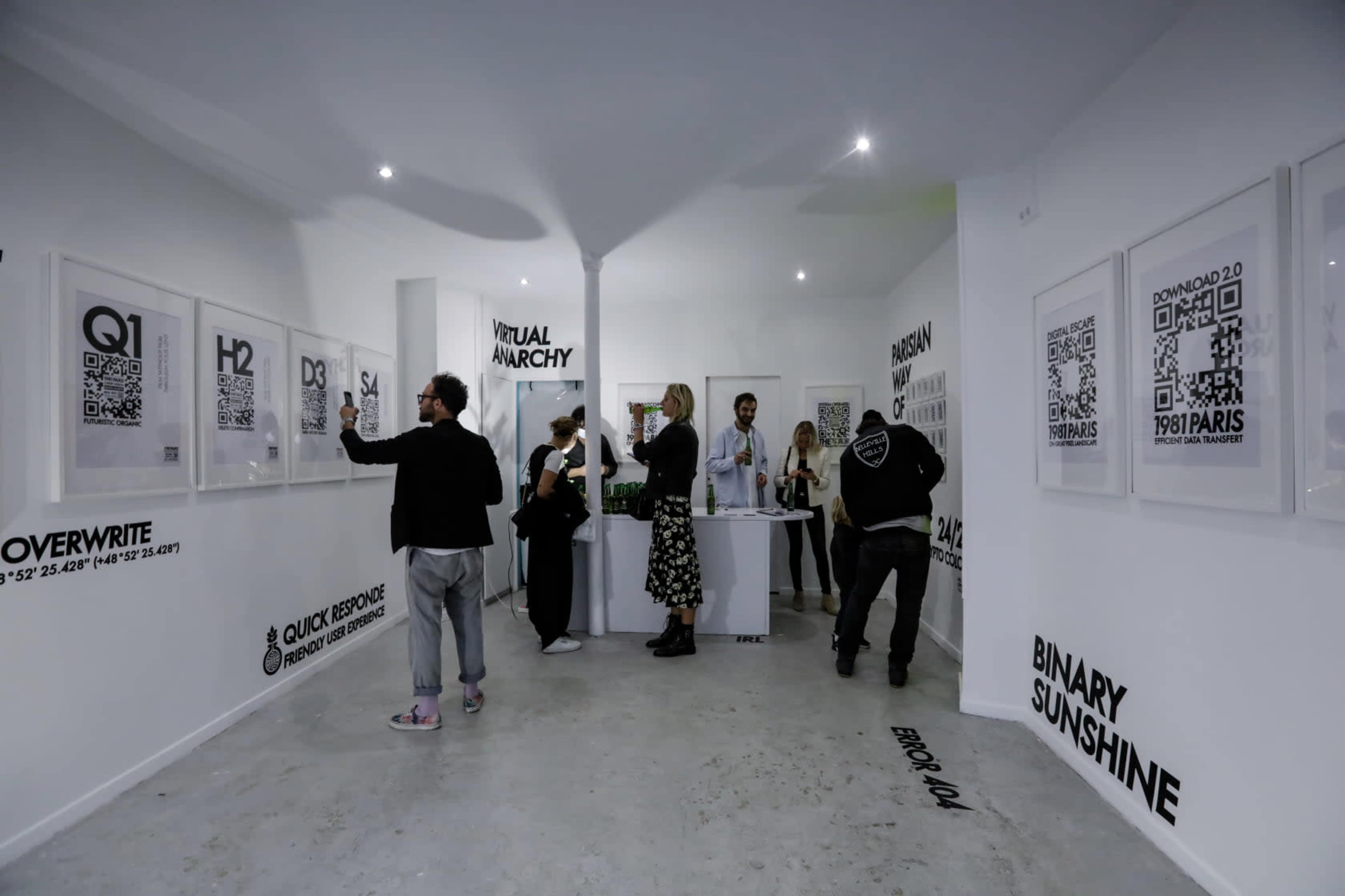 A group of people examines framed artworks displayed on the walls of a contemporary gallery with minimalist decor.