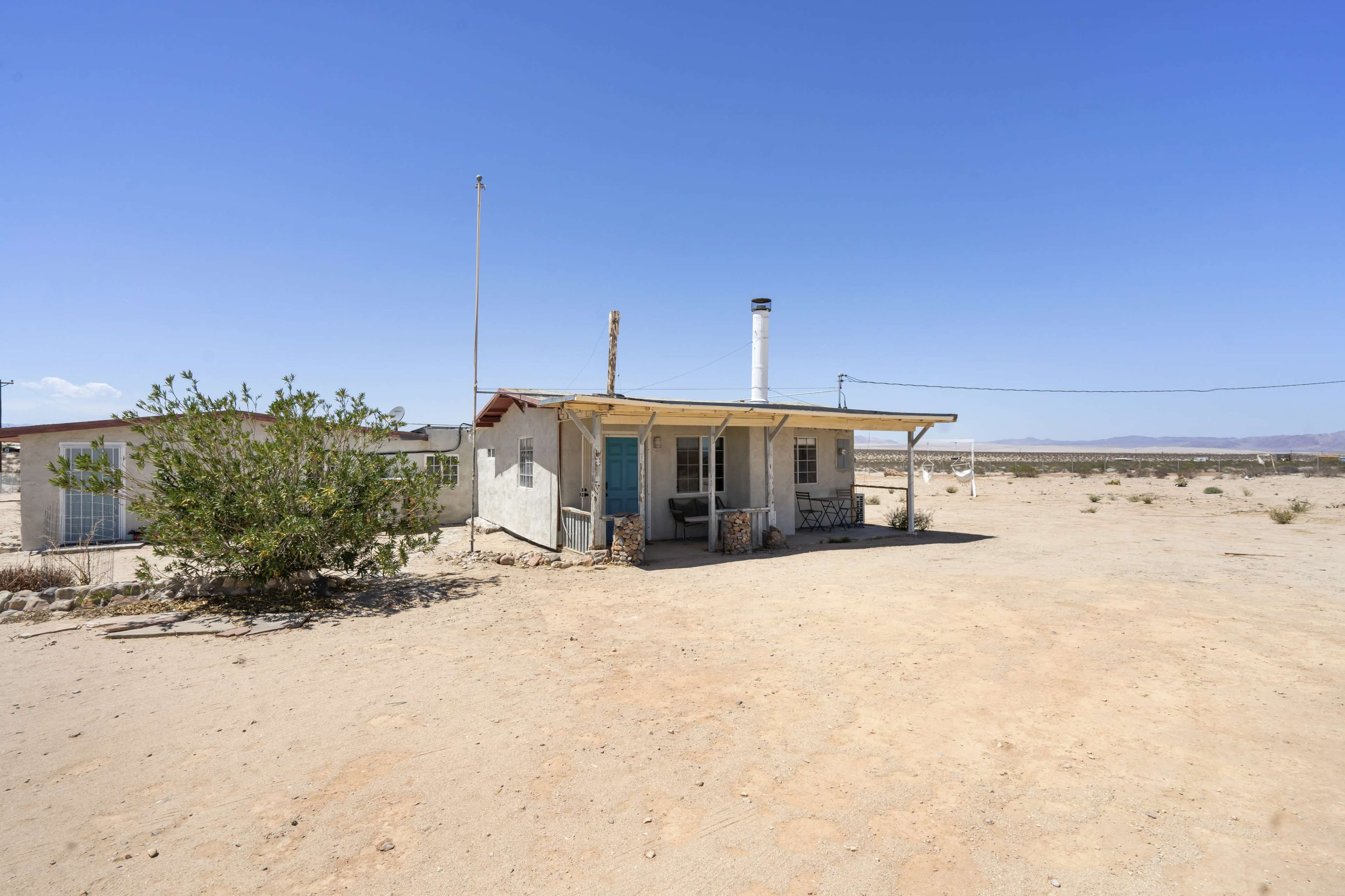 A small, single-story house with a blue door and a chimney sits in a barren desert landscape.