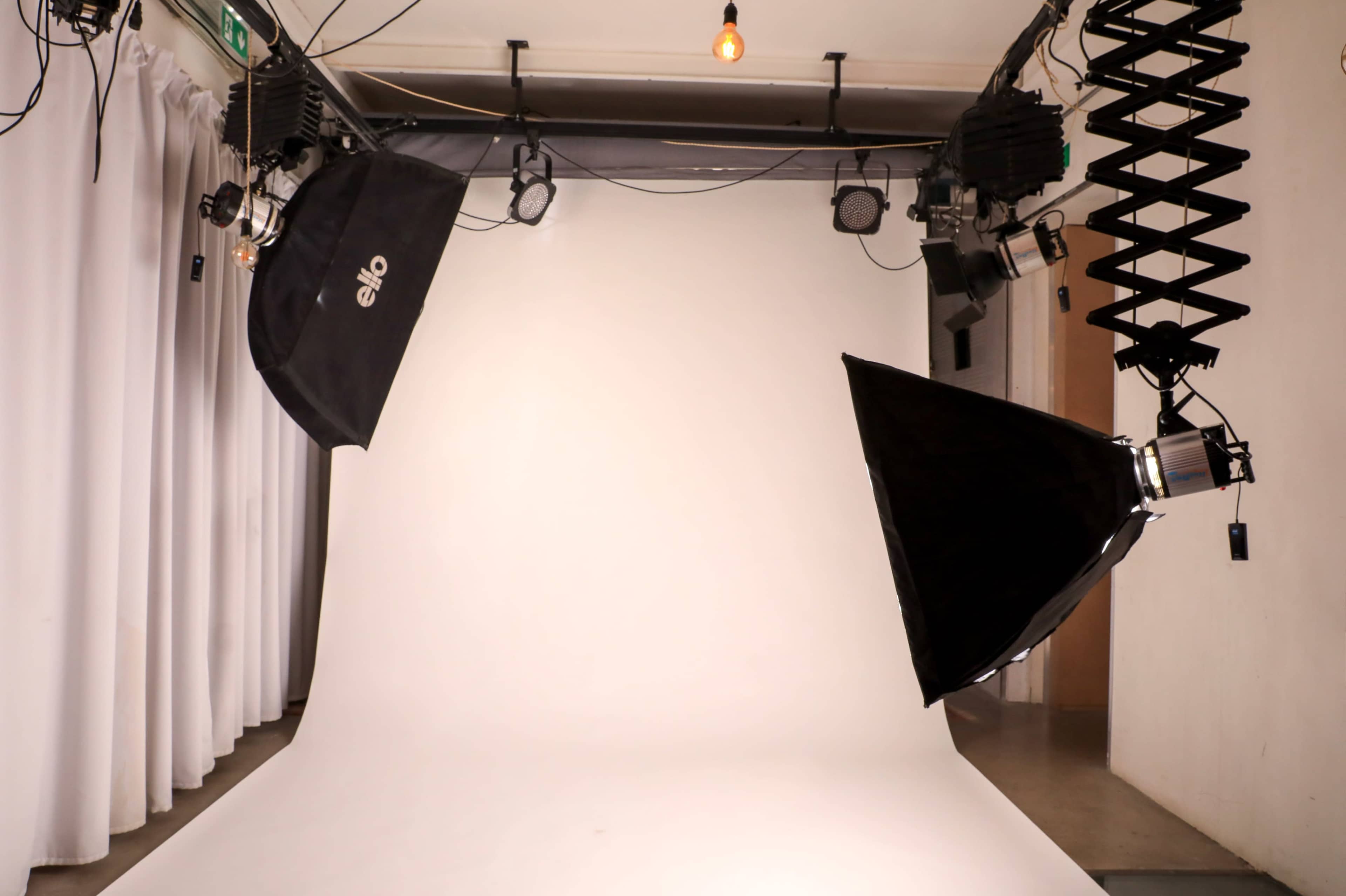 A photography studio features a seamless white backdrop with multiple light sources positioned above.