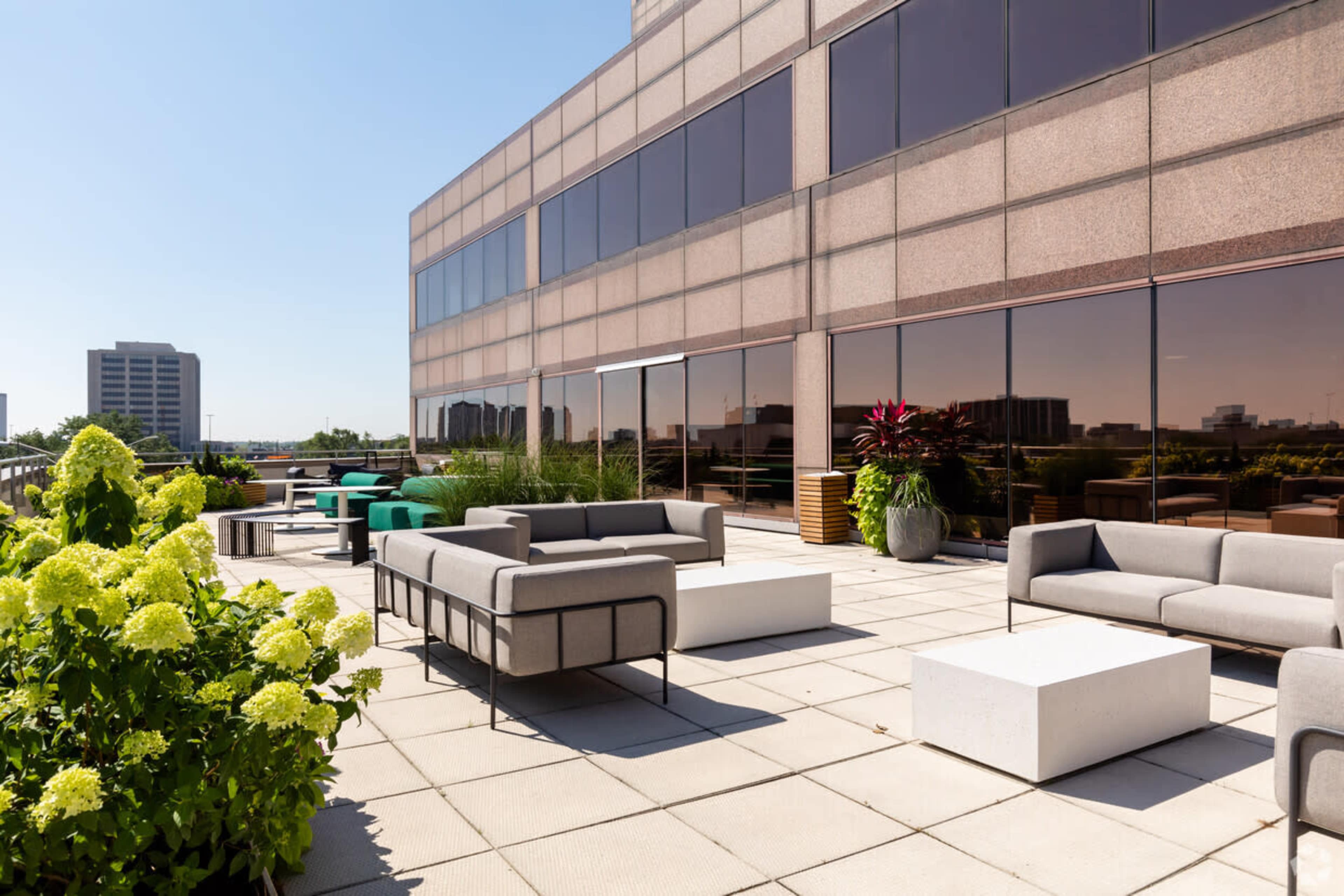 A spacious rooftop terrace features modern outdoor furniture and greenery against a backdrop of urban buildings.