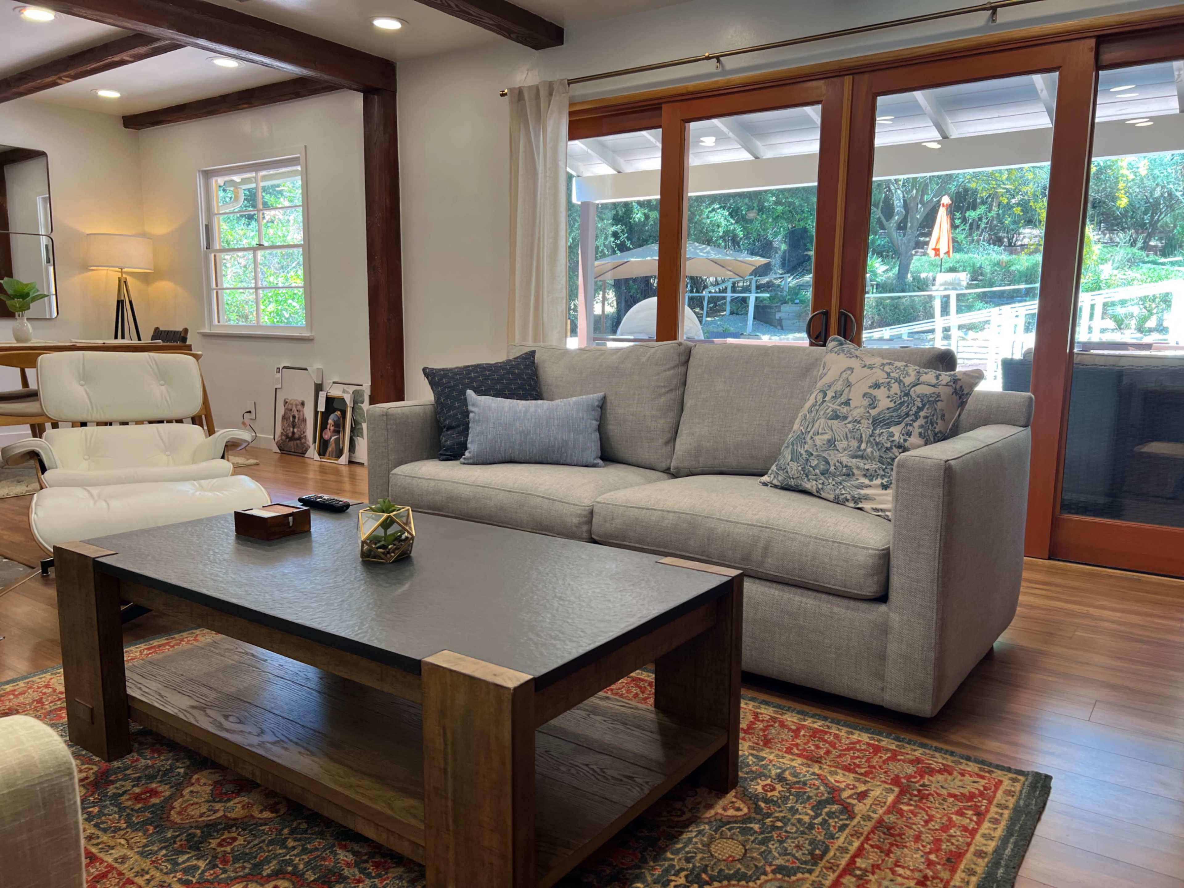 A light-filled living room features a gray sofa with decorative pillows, a wooden coffee table, and large glass doors opening to an outdoor space.