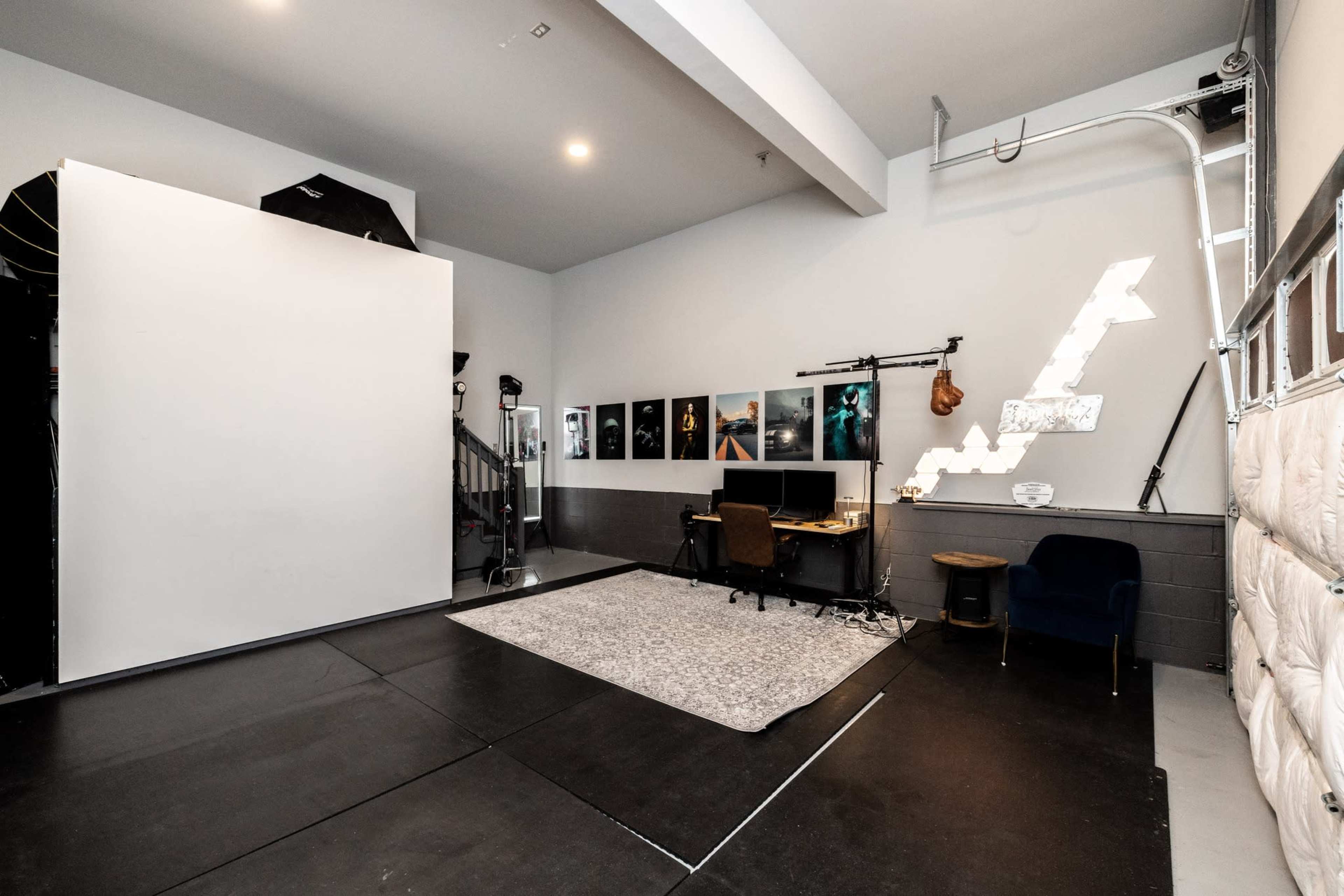 A spacious studio with a large white backdrop, a desk with a computer, and several framed pictures on the walls.