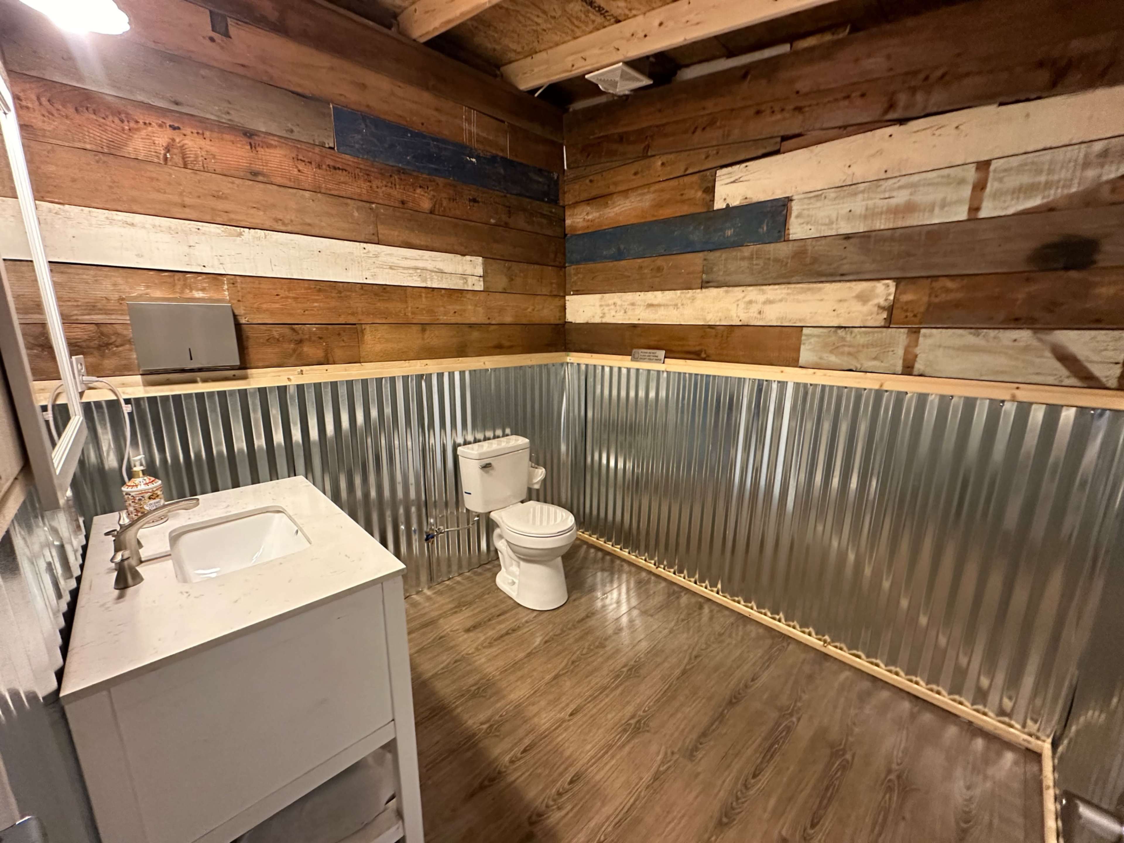 A rustic bathroom with wooden walls and a metal wainscoting, featuring a toilet and a sink.