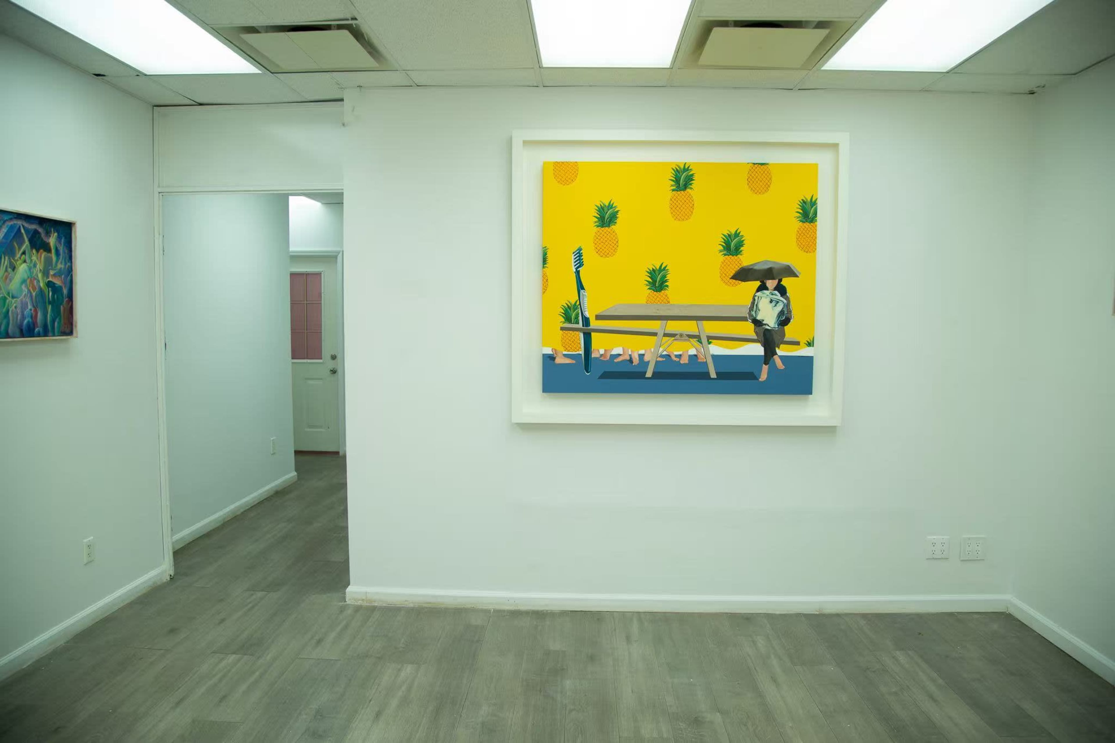 The image shows a brightly colored artwork featuring a dog under an umbrella against a backdrop of pineapples on a yellow wall in a white gallery space.