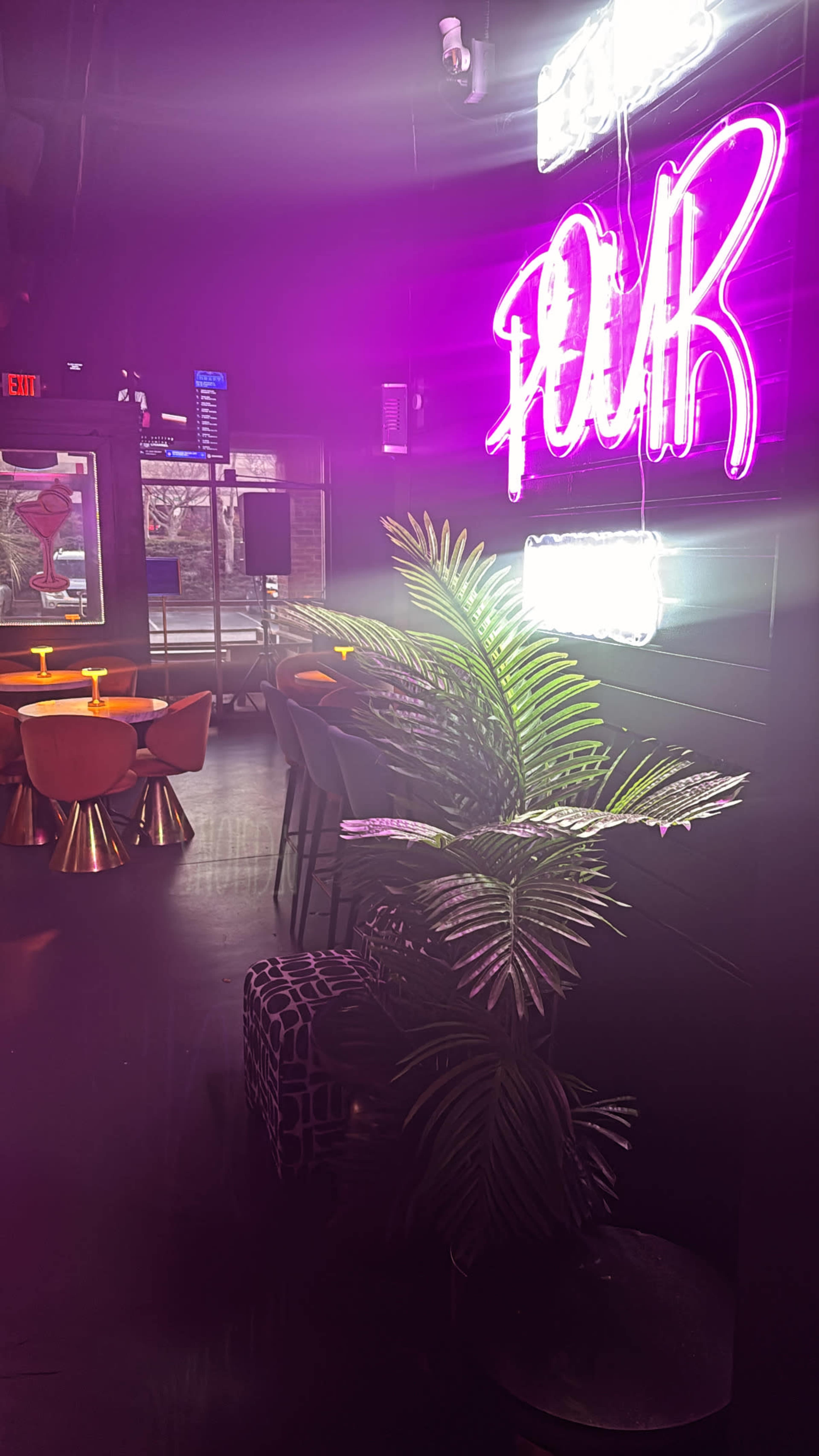 The image shows a modern bar interior with a neon sign that reads "FOUR," colorful seating arrangements, and a plant placed near the wall.