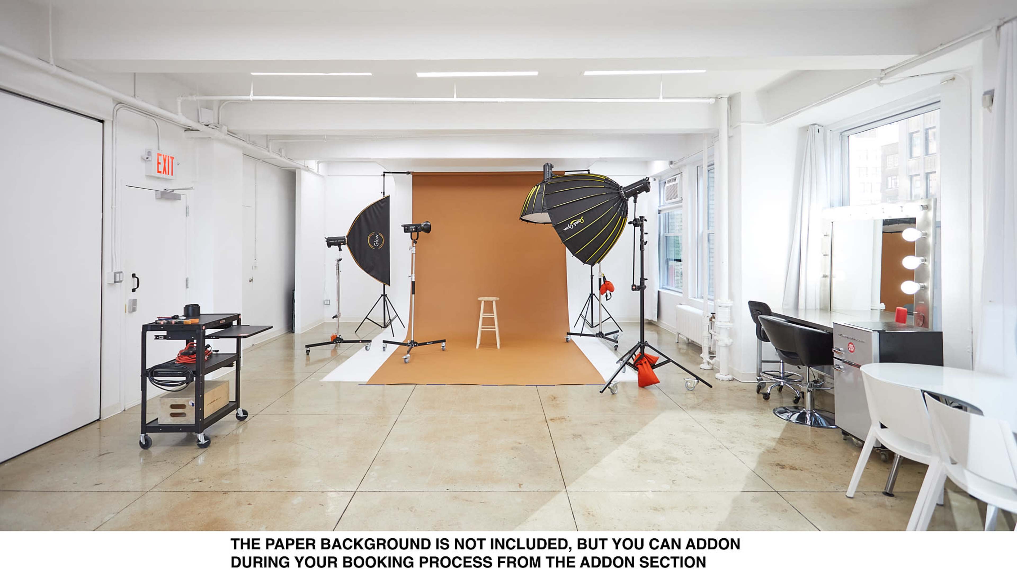 The image shows a photo studio with a brown backdrop, a stool, lighting equipment, and a makeup station with mirrors.