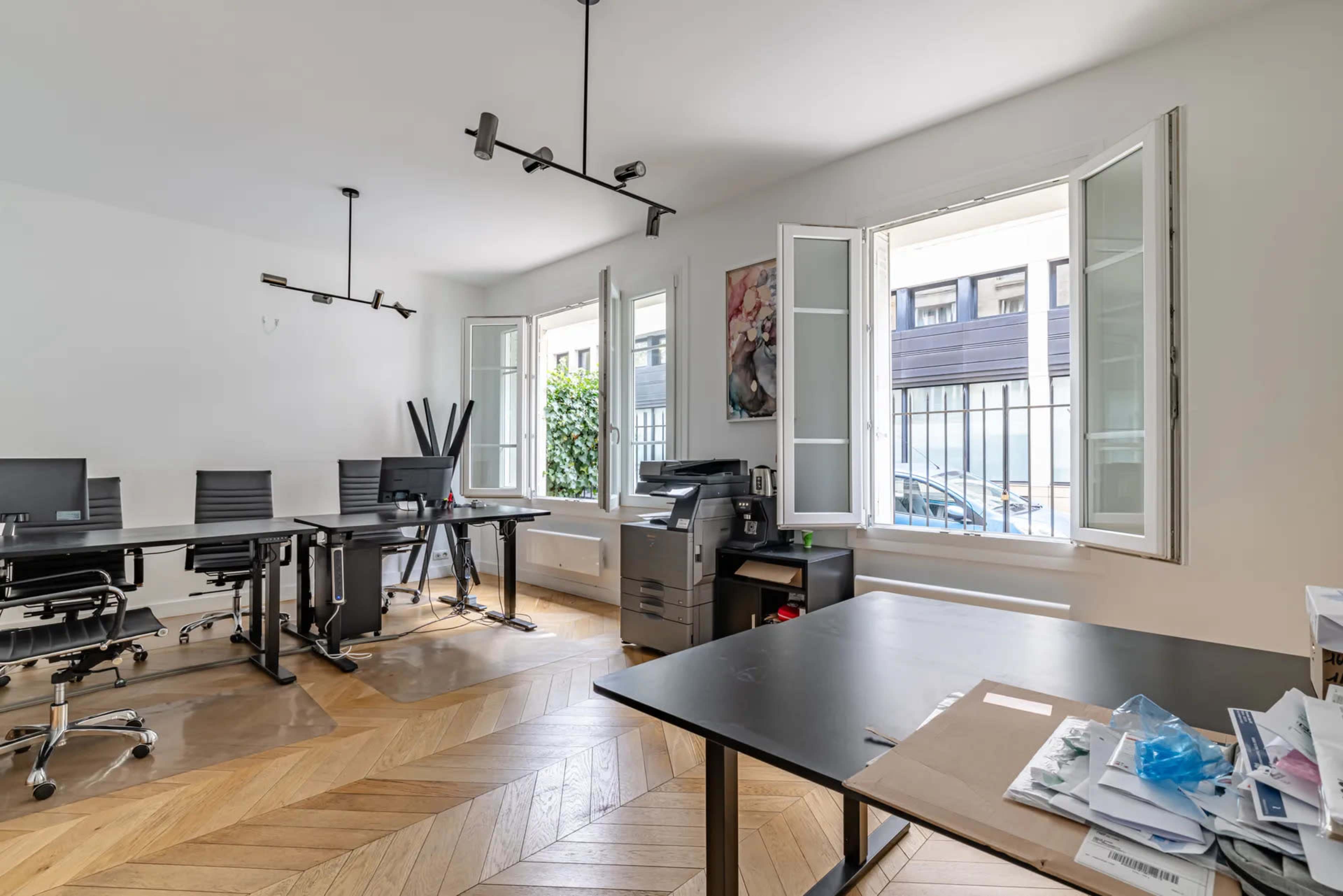 The image shows a modern office space with several black chairs, desks, and large windows that open to a street view.