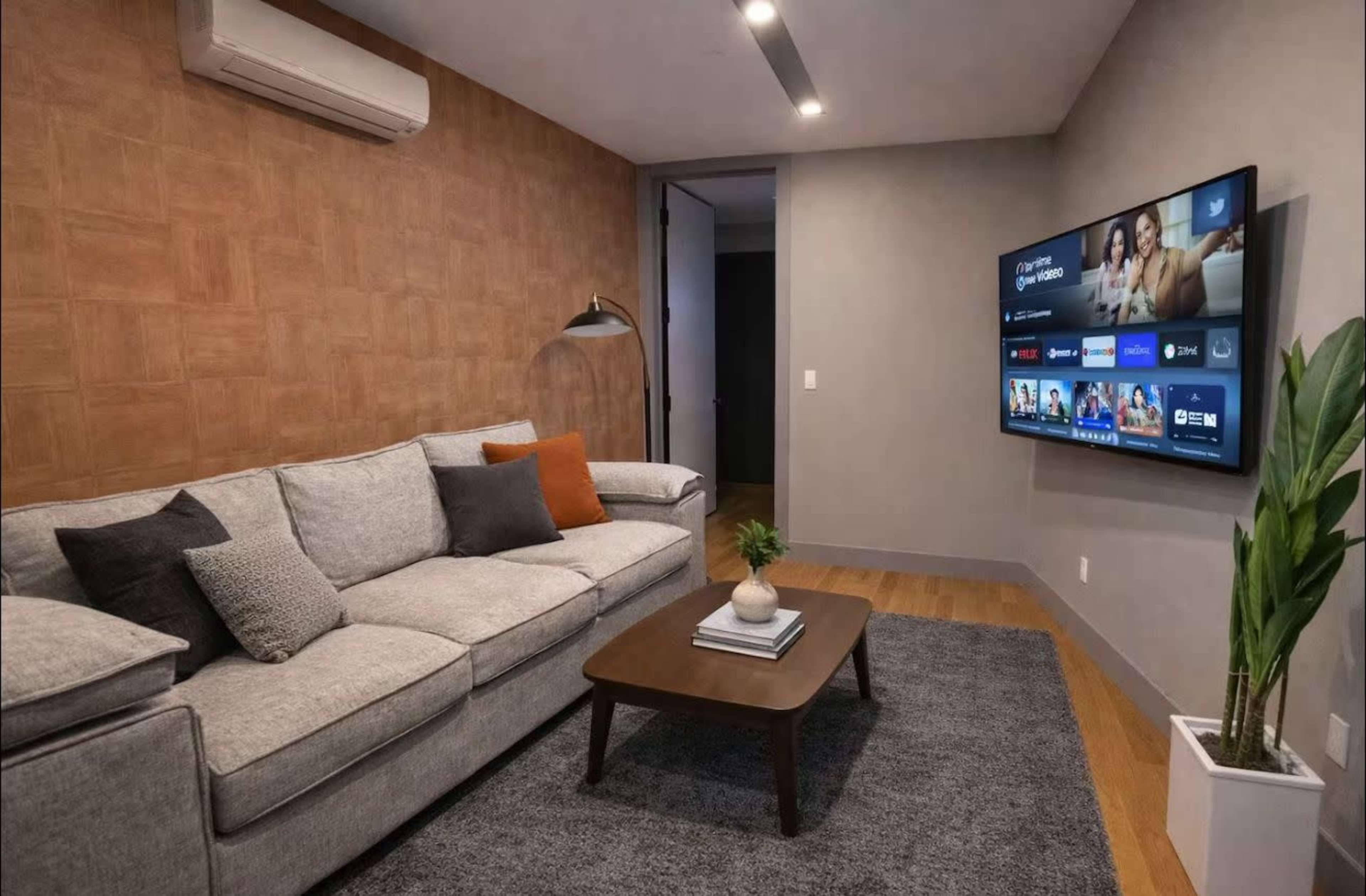The image shows a modern living room with a grey sofa, a wooden coffee table, a television mounted on the wall, and a plant in a white pot.