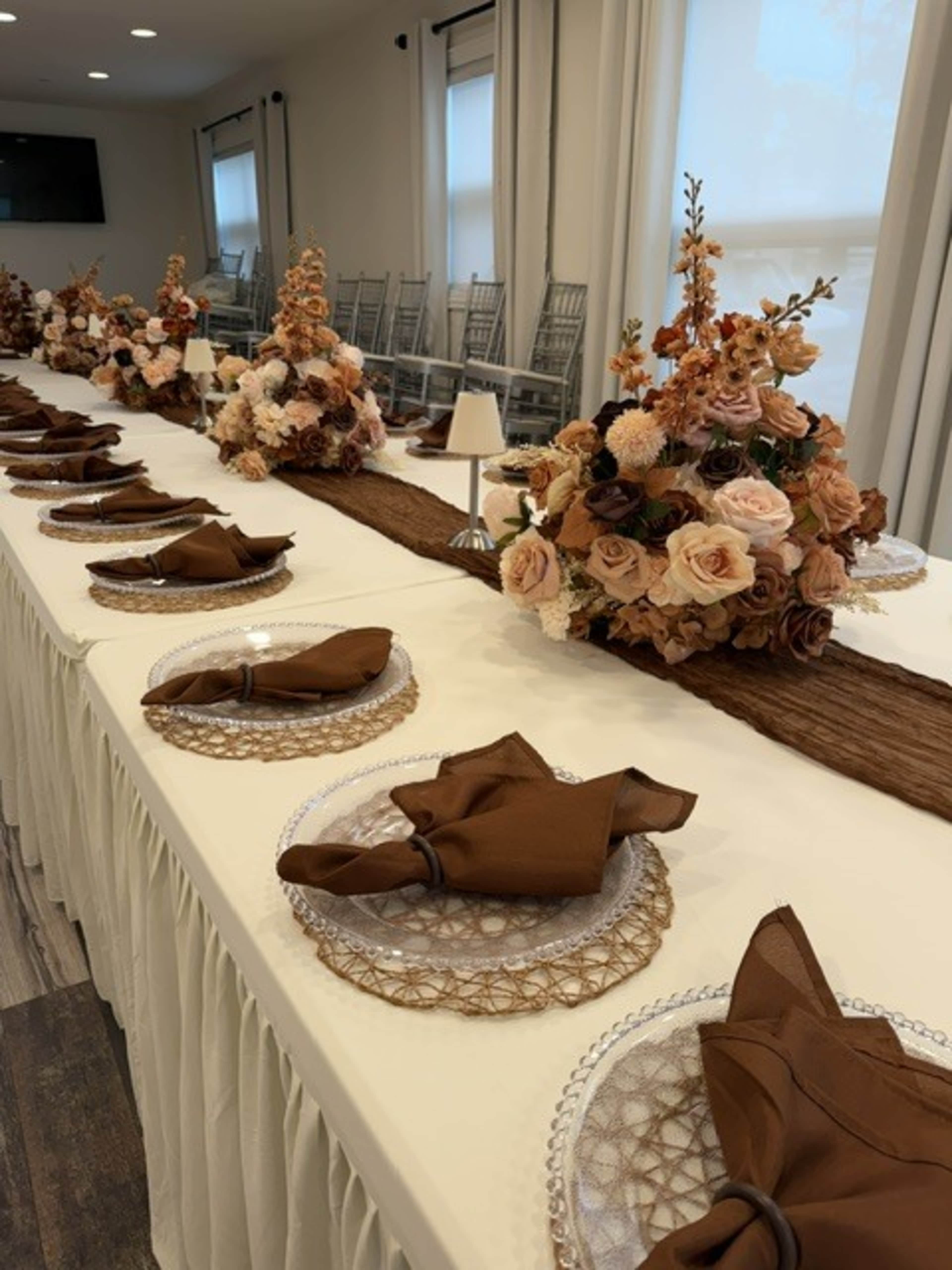 A long banquet table is set with elegant place settings featuring brown napkins and decorative floral centerpieces.