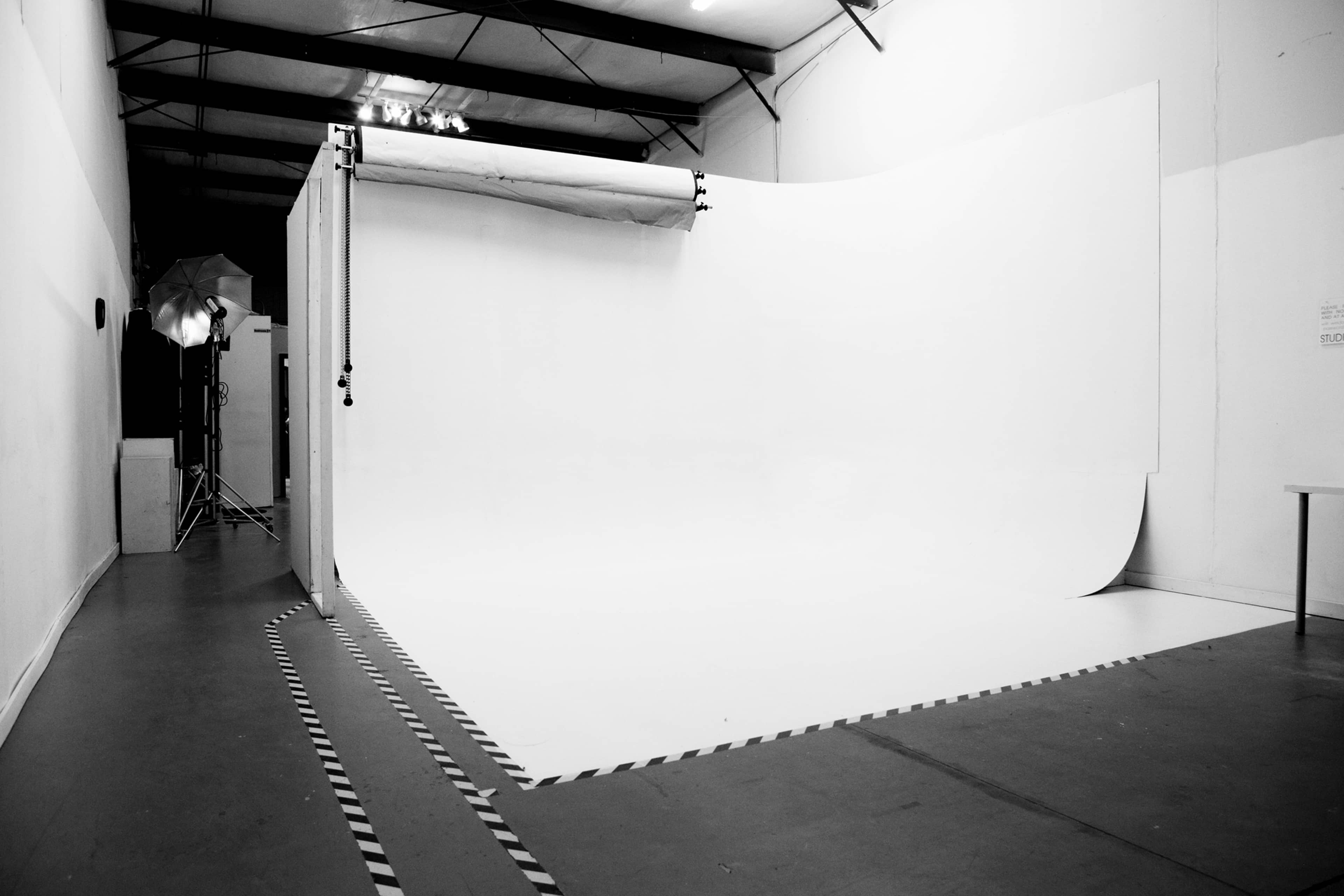A photography studio with a large white backdrop and a smooth floor, illuminated by studio lights.