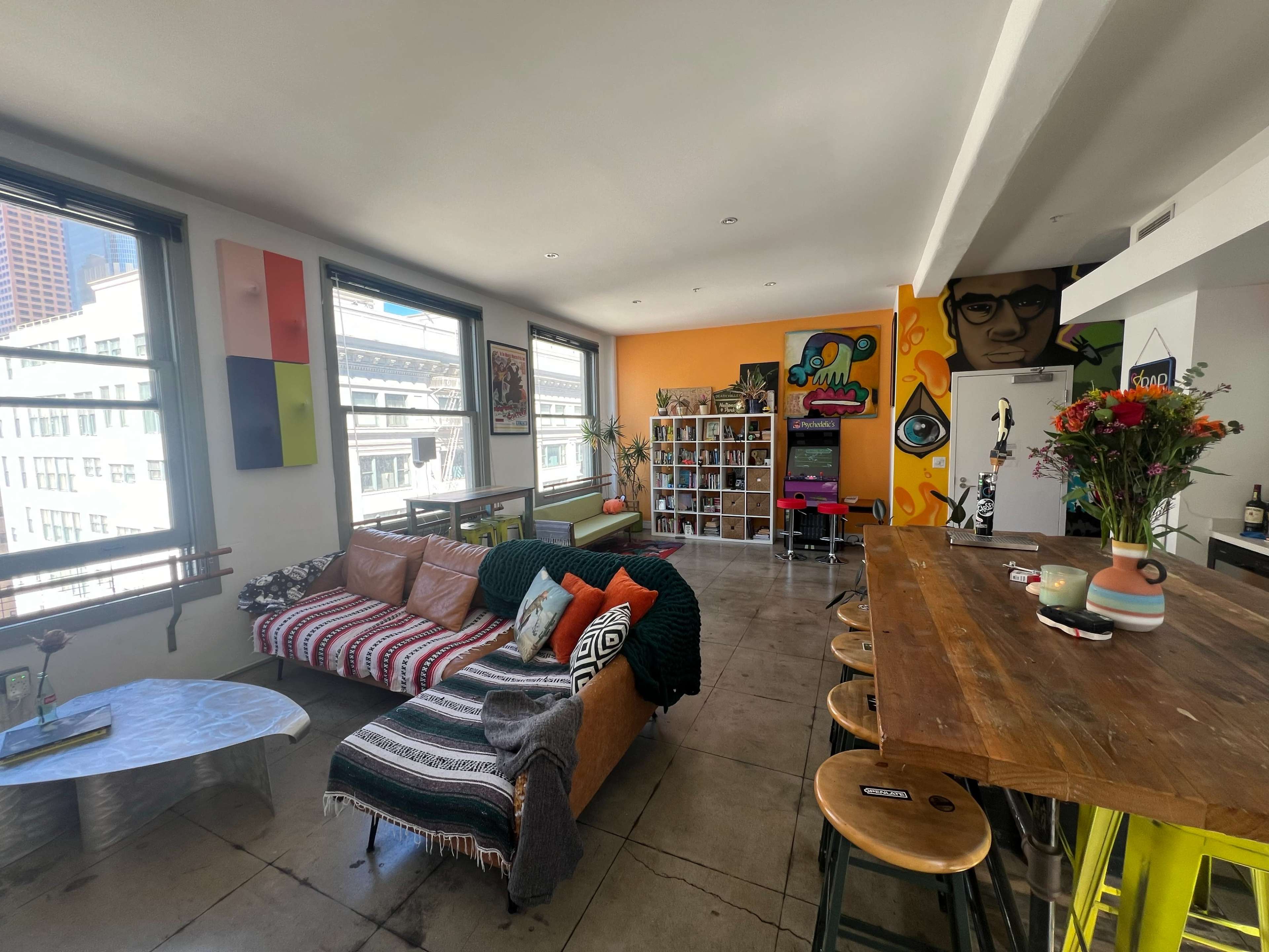 A modern apartment with a living area featuring a colorful couch, a dining bar, and vibrant wall art.