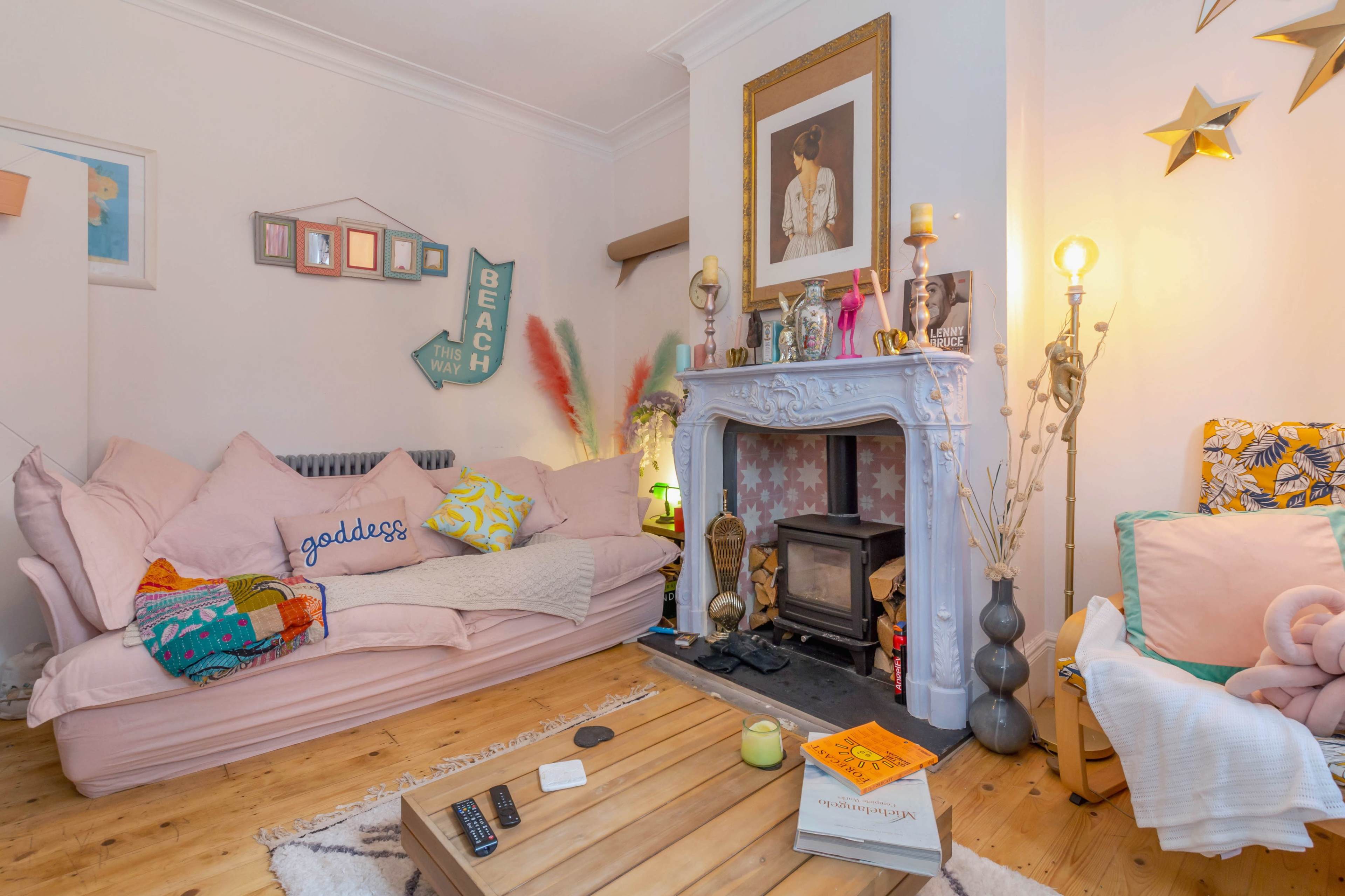 The living room features a light pink sofa, a decorative fireplace with a wooden coffee table, and various art pieces and decor arranged around the space.