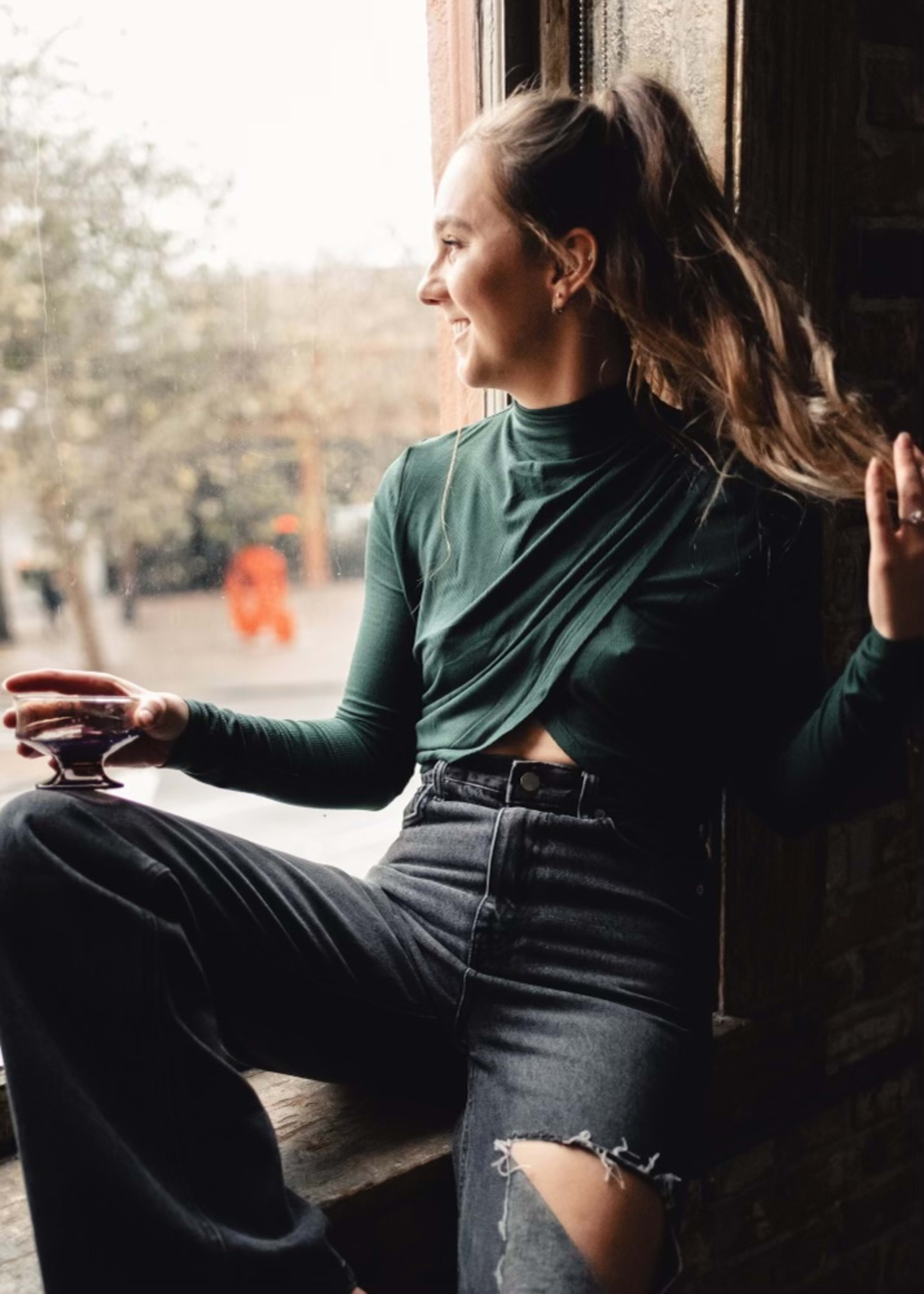 A fashion photo shoot with a woman sitting on a window sill with her hair in the wind.