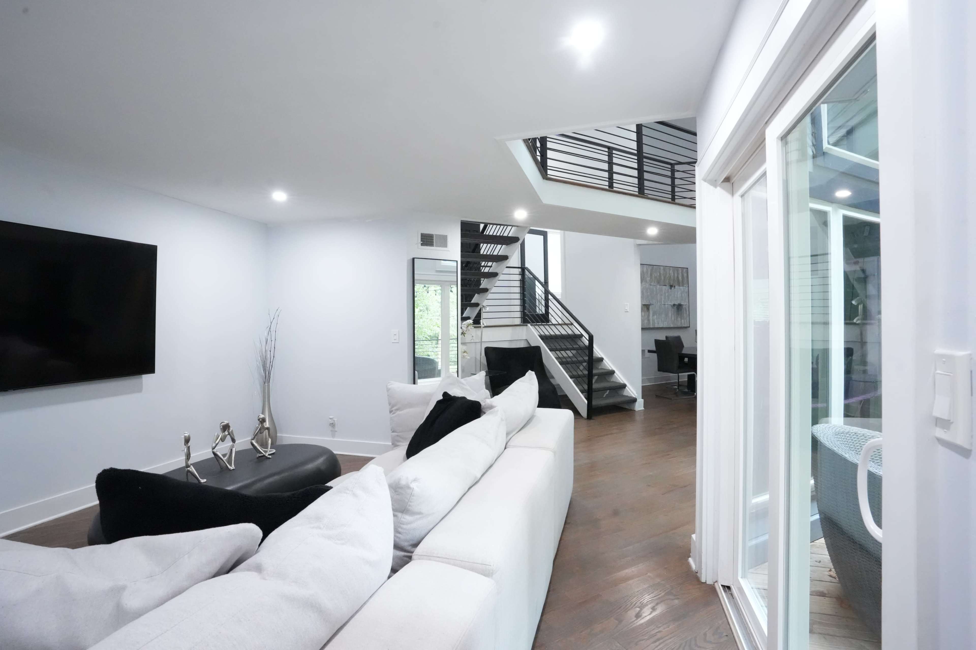 The image shows a modern living room with a light blue wall, a large sectional sofa, and a staircase leading to an upper level.